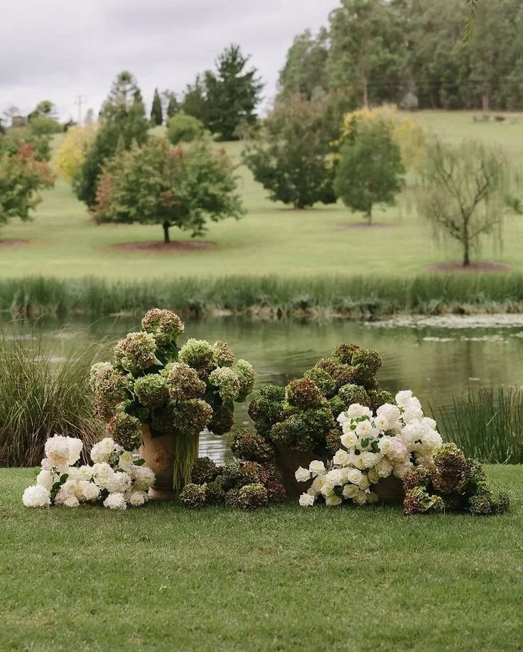 A wedding ceremony floral display infront of a lake , with a collection of hydrangeas and white roses. Niagara wedding Flowers