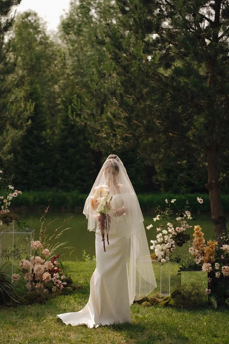Bride standing infront of lake during wedding ceremony with blush and brown flower arrangements. muskoka wedding flowers