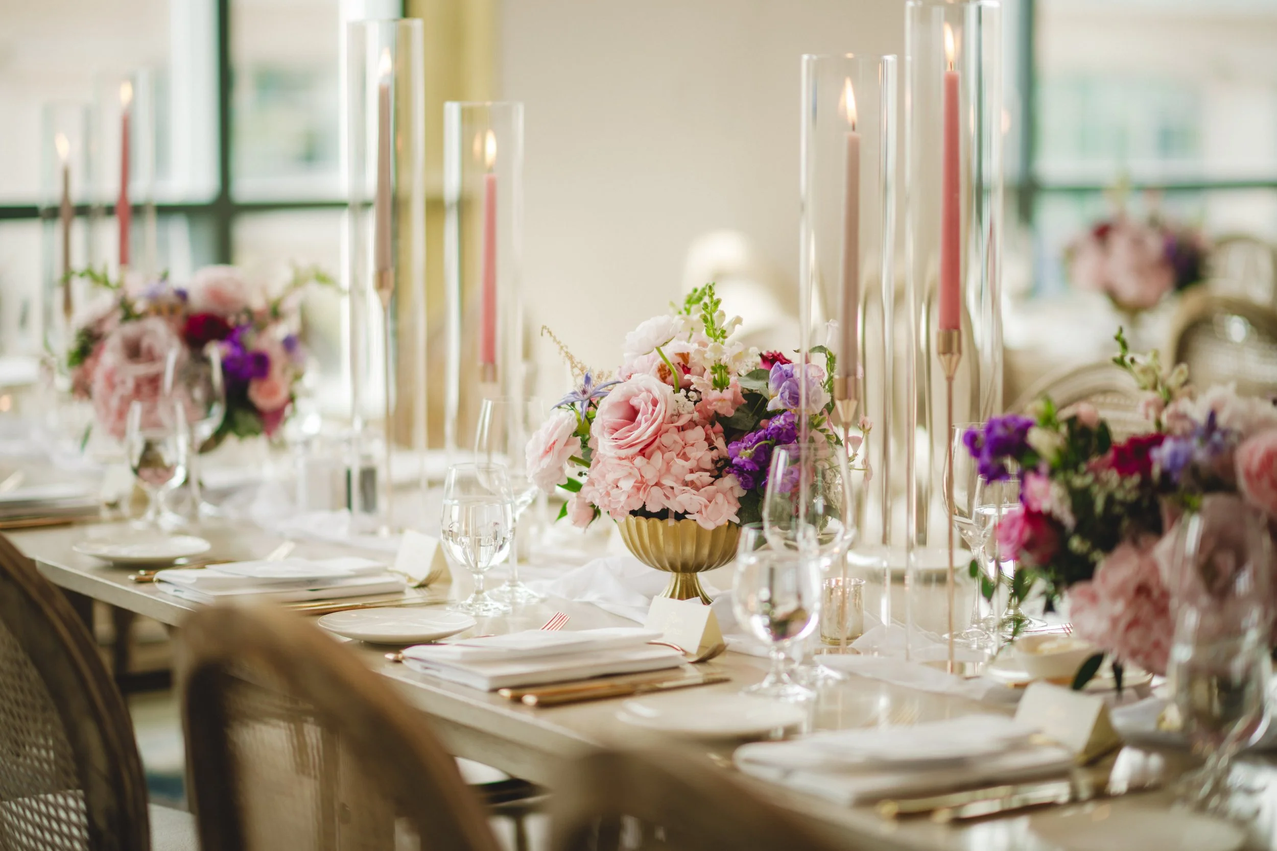 Pink and purple floral centrepieces with gold compotes and taper candles at a Pearle Hotel and Spa wedding reception.
