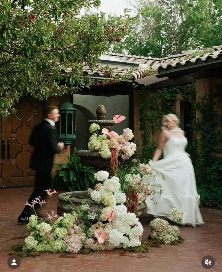 A bride a groom running around a fountain with a cascading floral arrangement, ontario wedding flowers