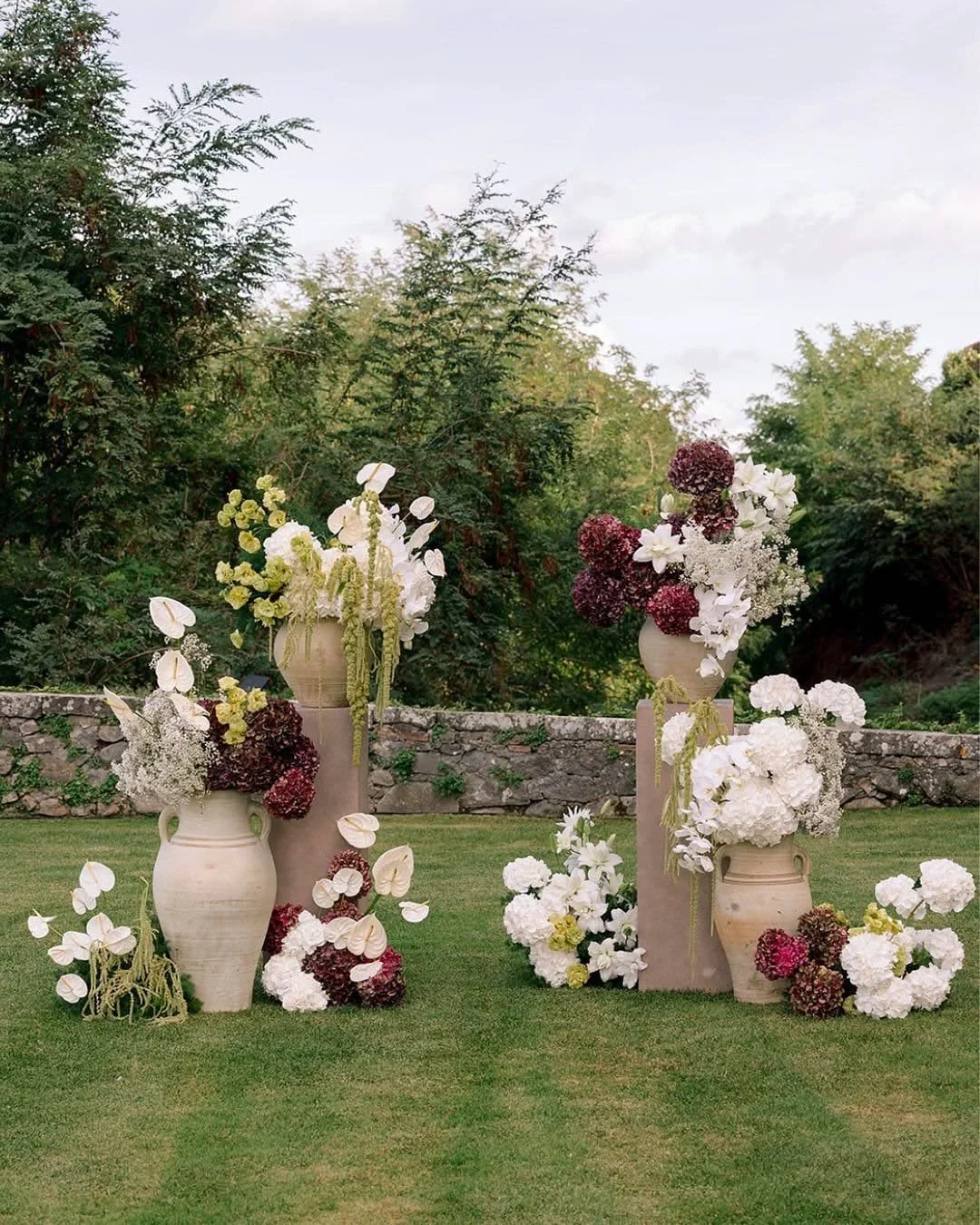A collection of white, burgundy, and green wedding ceremony floral arrangements on pedestals. Bride and bridesmaids in burgundy wedding dresses with calla lily bouquet. Hamilton wedding Flowers
