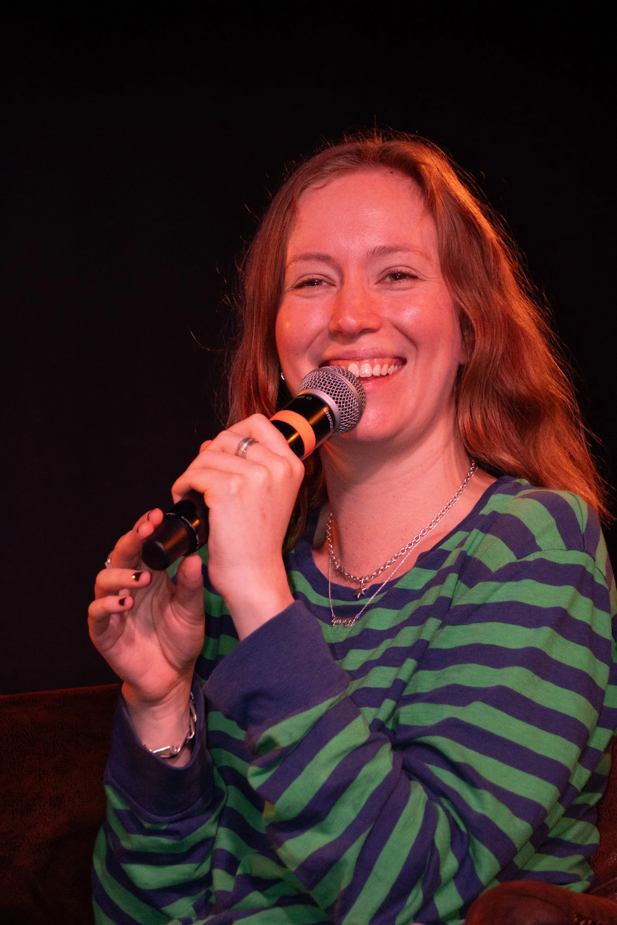 A woman with red hair smiling and holding a microphone during a performance or event.