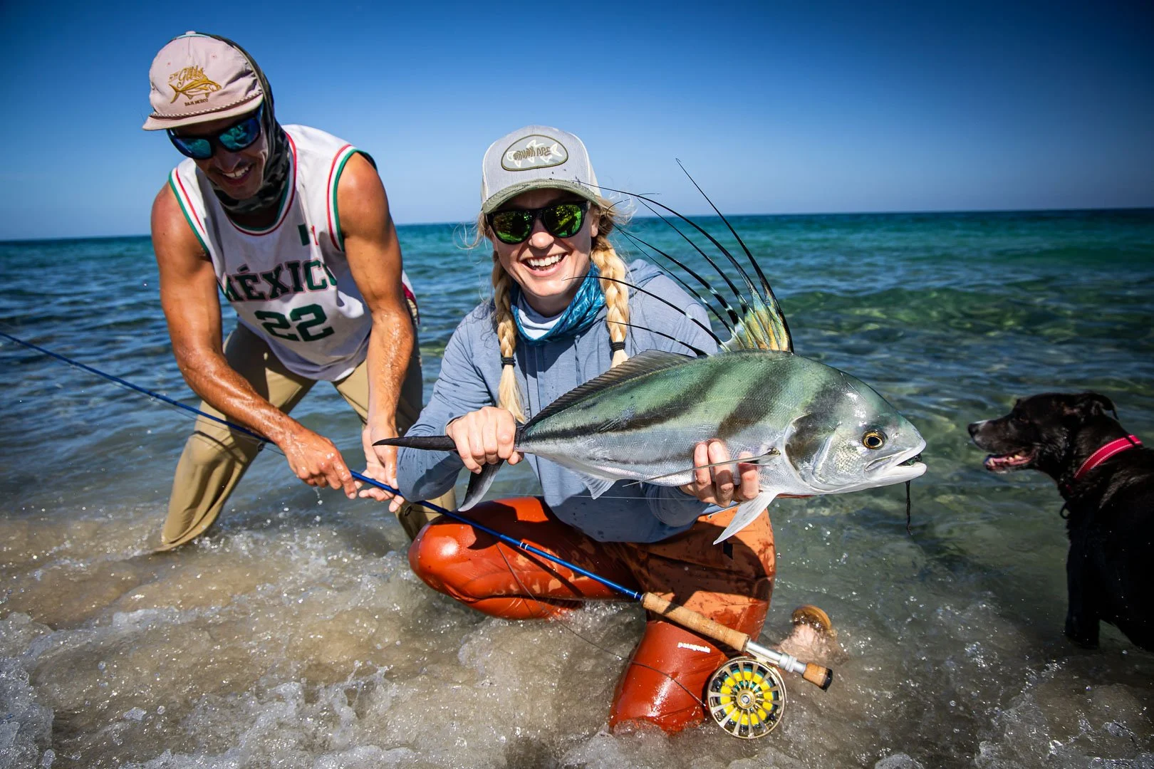 Two people holding a Roosterfish with a dog in Baja, Mexico