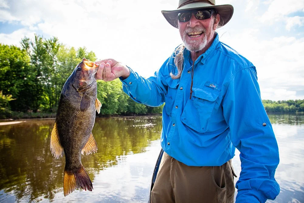 Smiling angler holding a smallmouth bass he caught while on a guided fishing trip with Black Earth Angling Co.