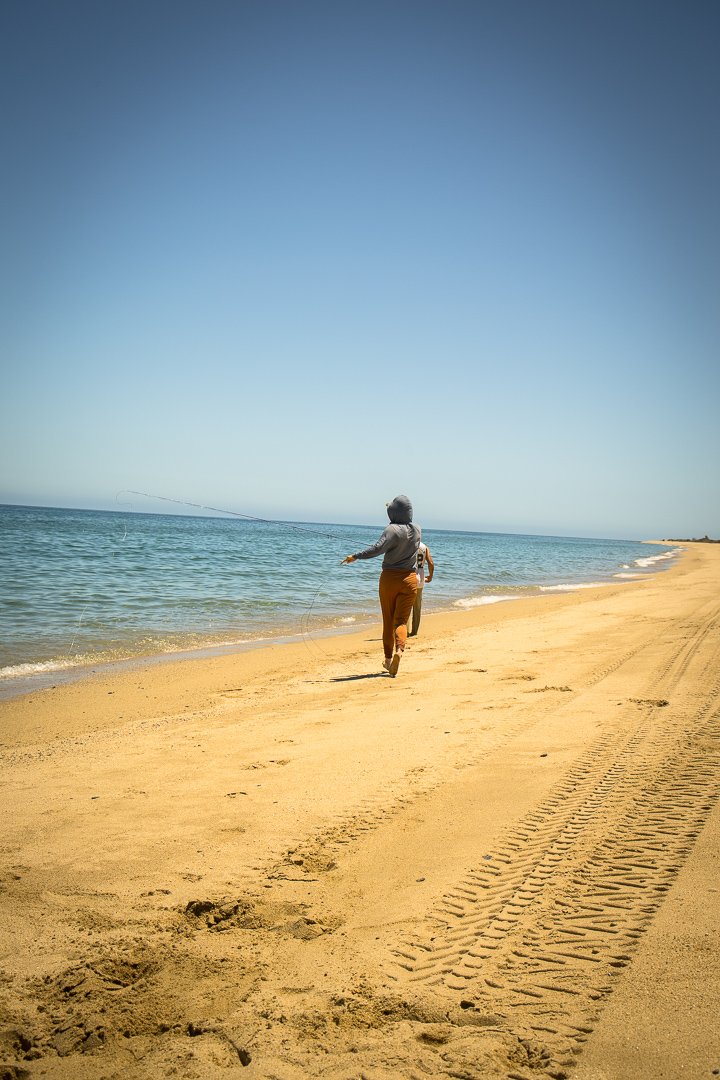 A woman running down a beach in Baja casting to a Dorado