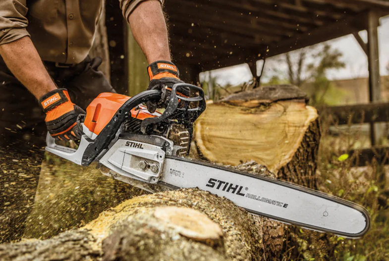 Person using a Stihl chainsaw to cut a large piece of wood outdoors, with sawdust flying.
