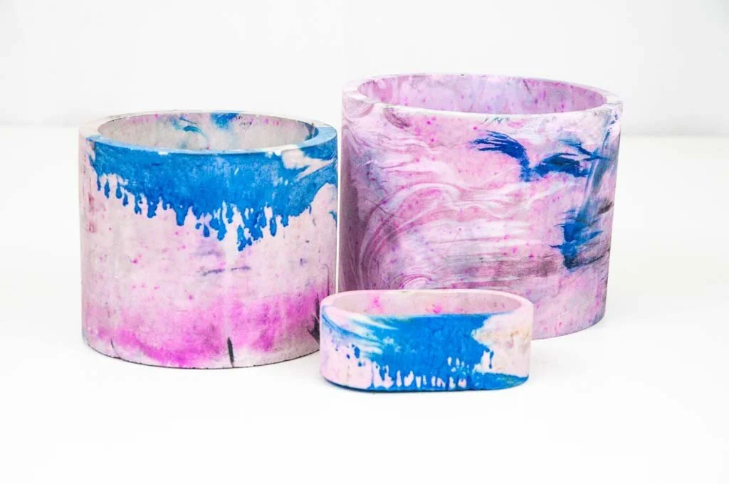 Three cylindrical planters with pink, white, and blue marbled design placed on a white surface.
