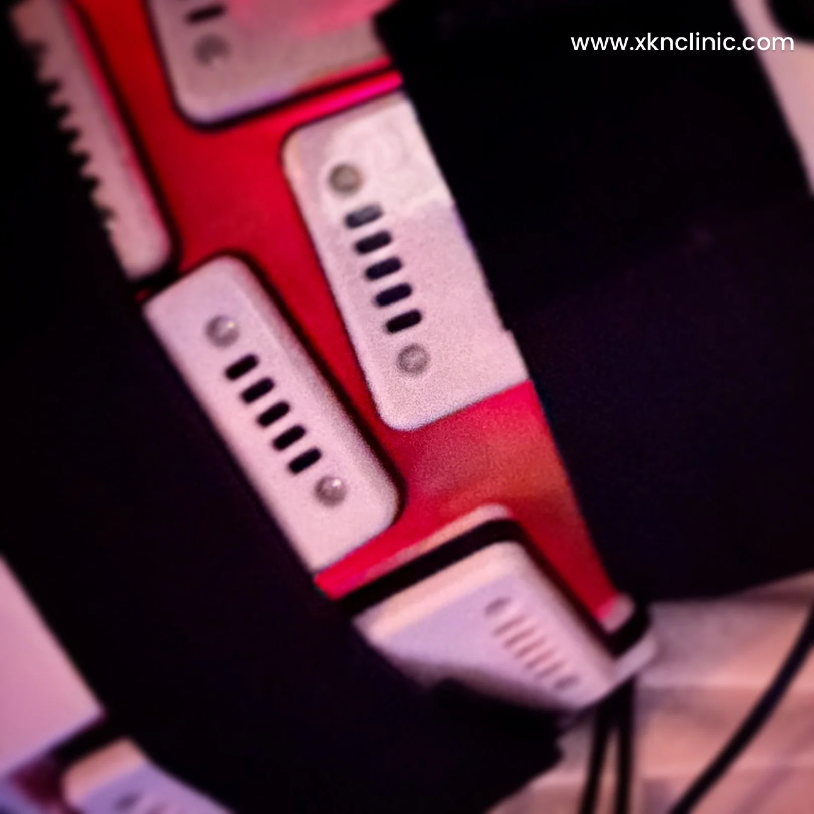 Close-up image of a medical or technological device with multiple white connectors and a red body, displaying an URL www.xknclinic.com in the top right corner.