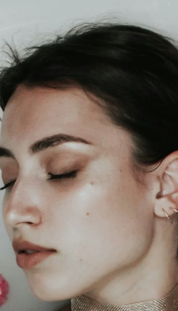 Close-up of a woman with dark hair, closed eyes, and earrings, facing left with a calm expression.