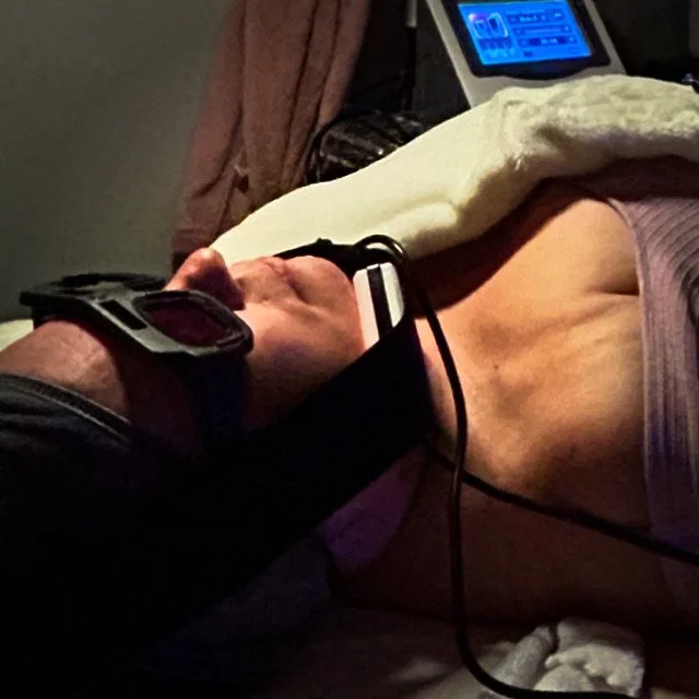 Person lying on a bed undergoing a medical or cosmetic treatment, with various electronic devices and cords connected to them.