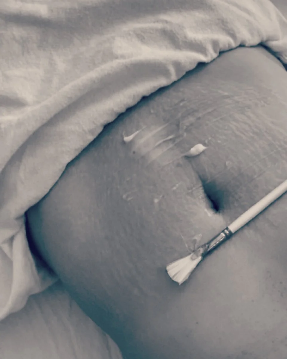 A close-up of a belly with a belly button, with a small paintbrush resting on it, and a cloth draped around the area.