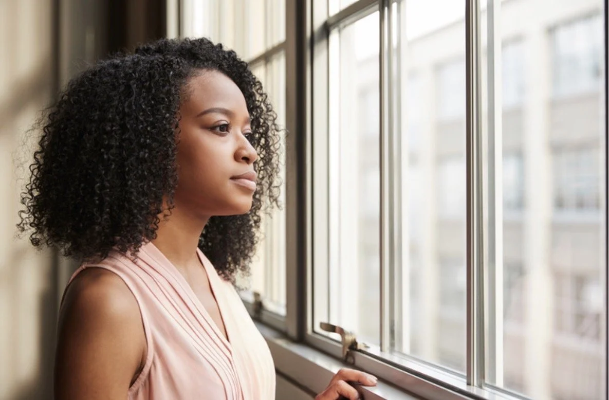 Woman looking out window with internal anxiety, representing high-functioning anxiety and emotional tension