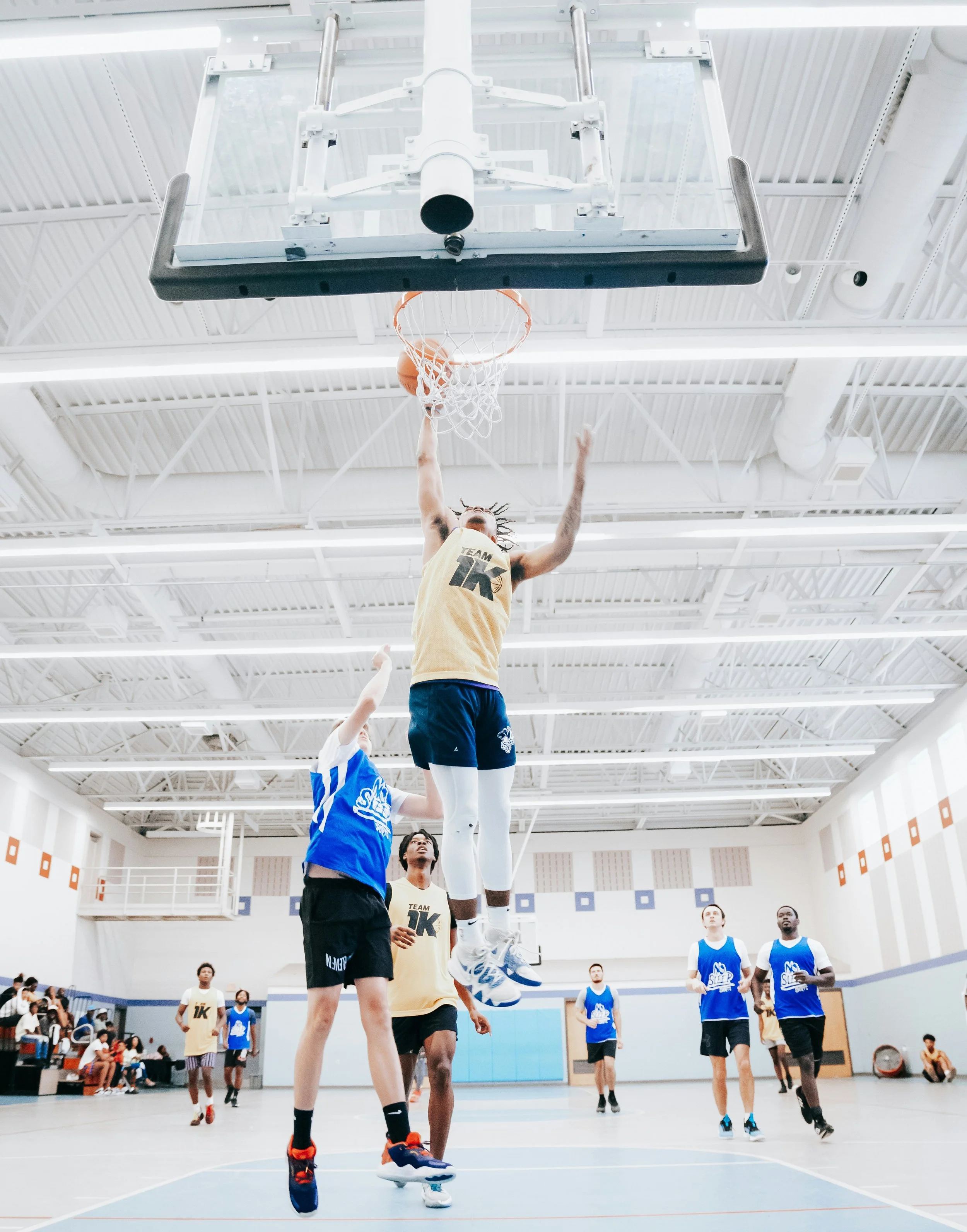 A basketball game in progress with a player jumping towards the hoop to score while others watch and play defense.