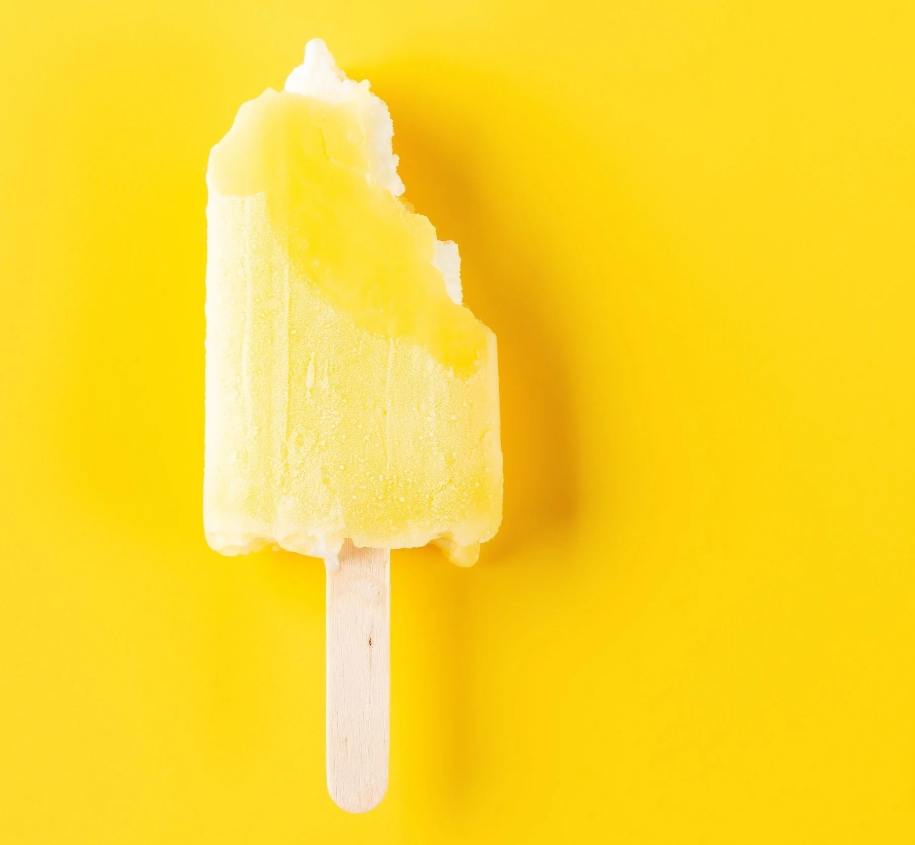 Close-up of a yellow popsicle on a yellow background.