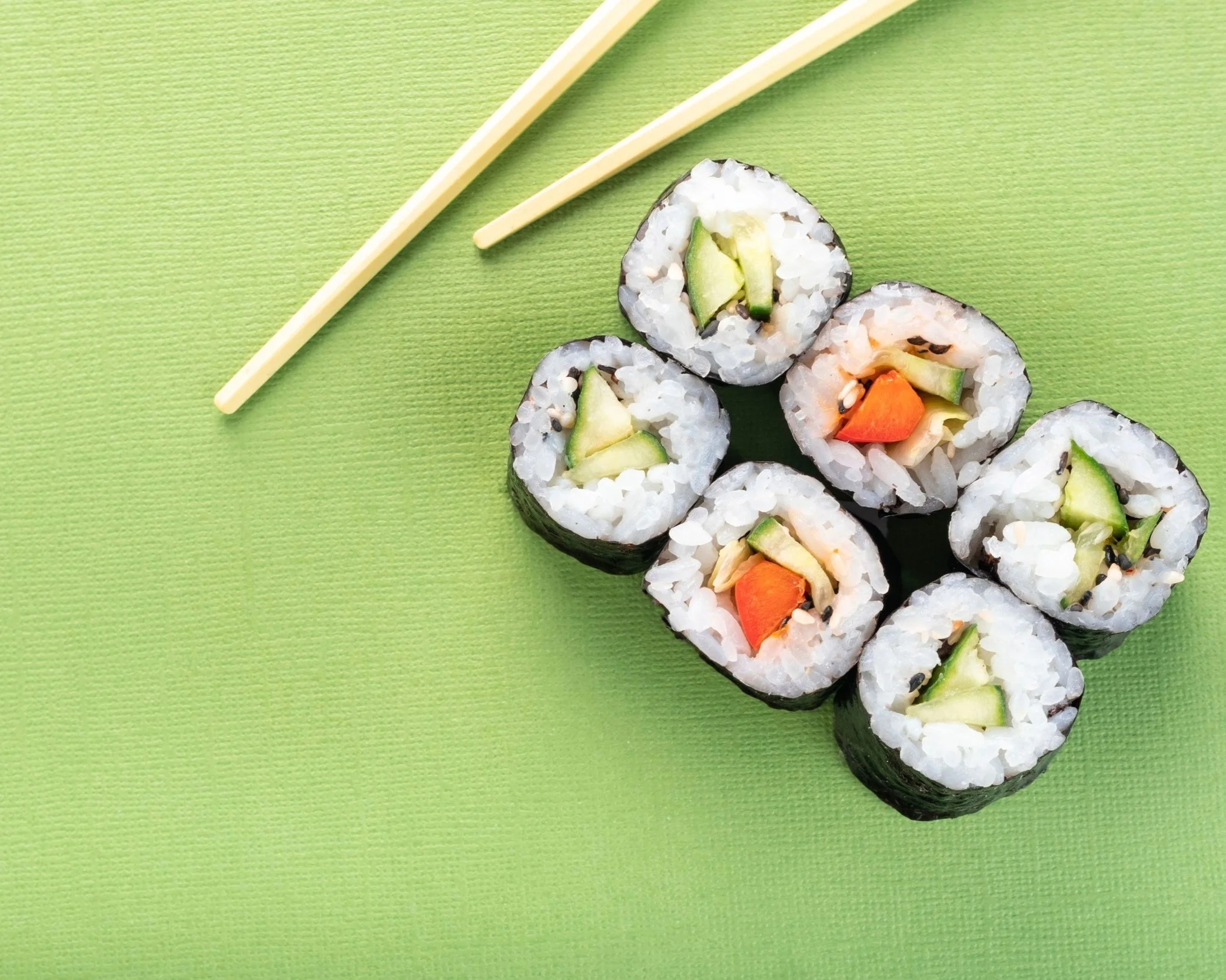 Six pieces of sushi rolls on a green surface with a pair of chopsticks nearby.