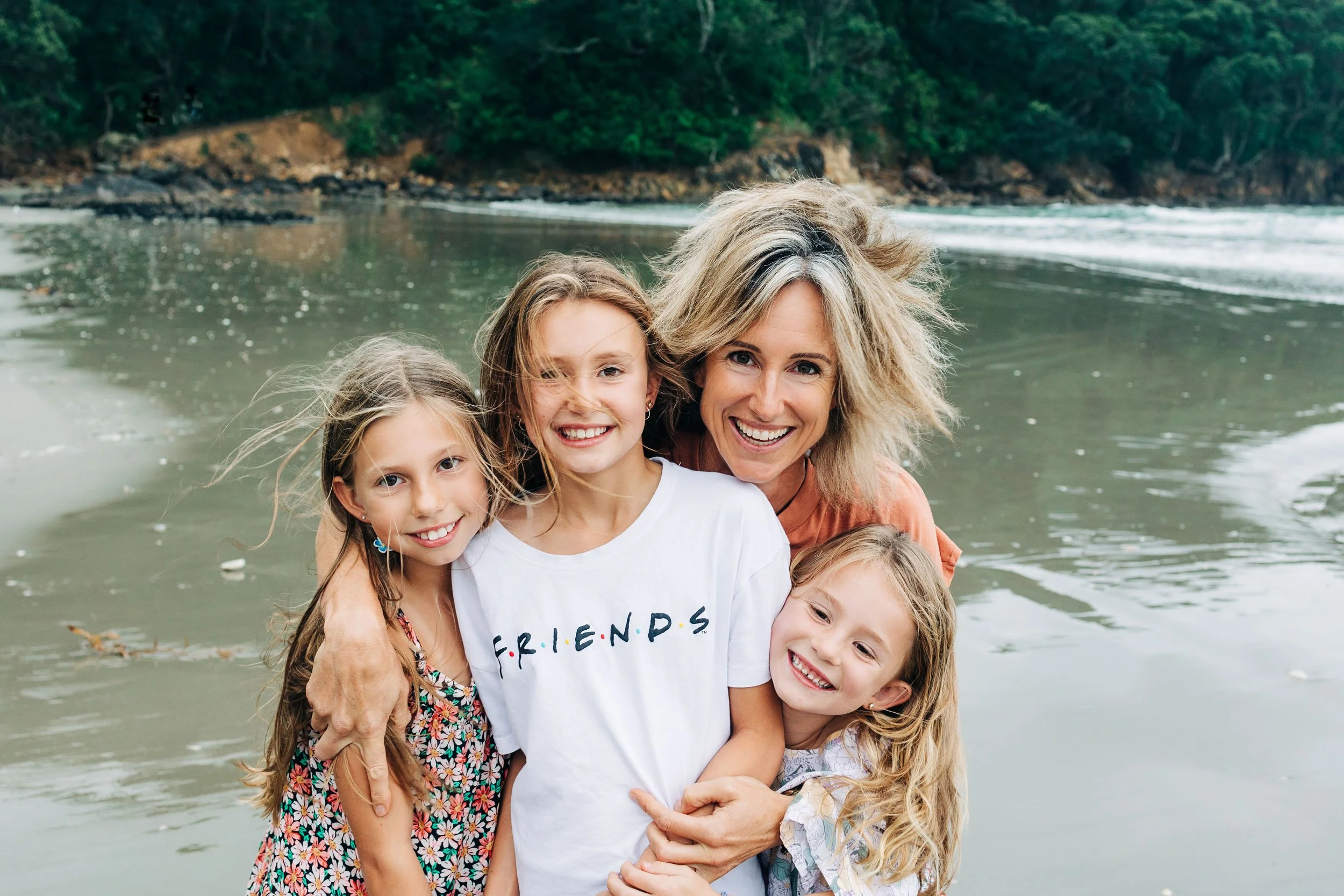 Jampacked Nutrition - Holly Murphy - A happy woman and four smiling young girls embracing on a beach with water and trees in the background.
