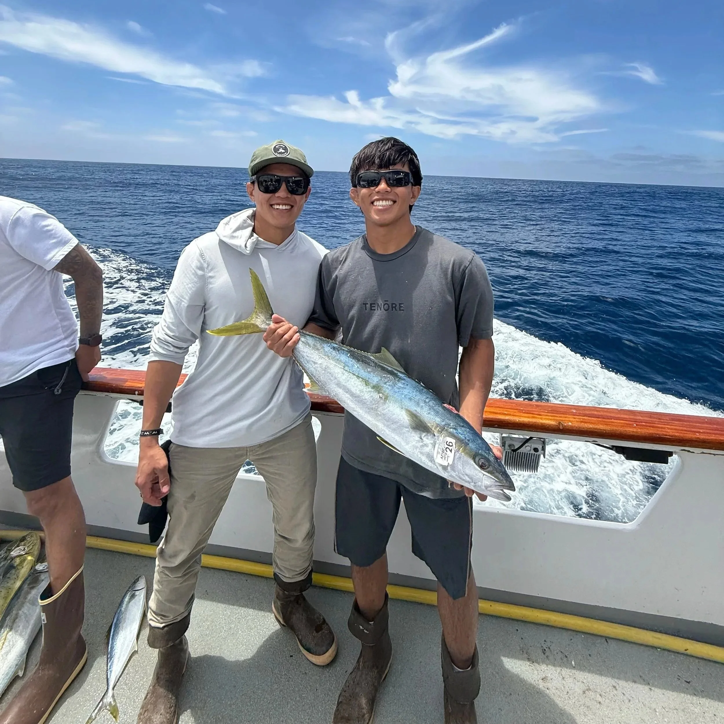 Two young men on a boat holding a fish, with a background of blue ocean and sky
