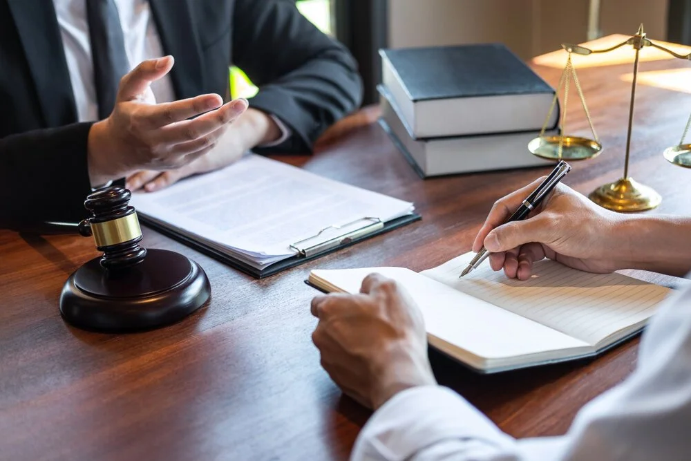 A lawyer explaining legal matters to a client during a consultation, with legal books, a gavel, and scales of justice on the table.