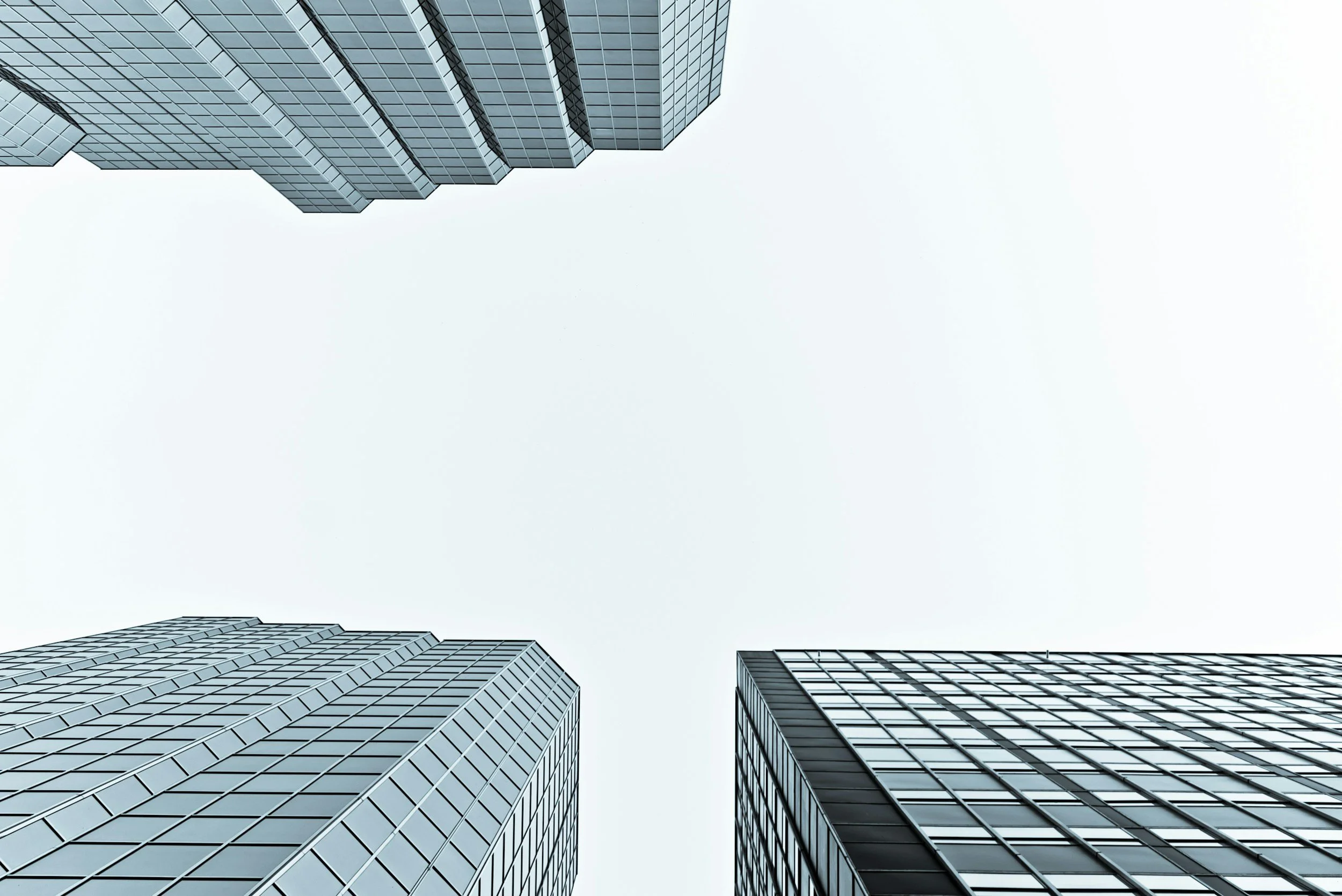 Looking up at tall modern glass skyscrapers against a pale sky.