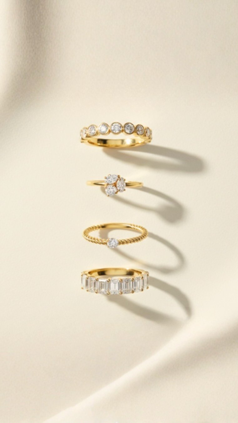 Four gold rings with diamonds arranged vertically against a light background, casting shadows.