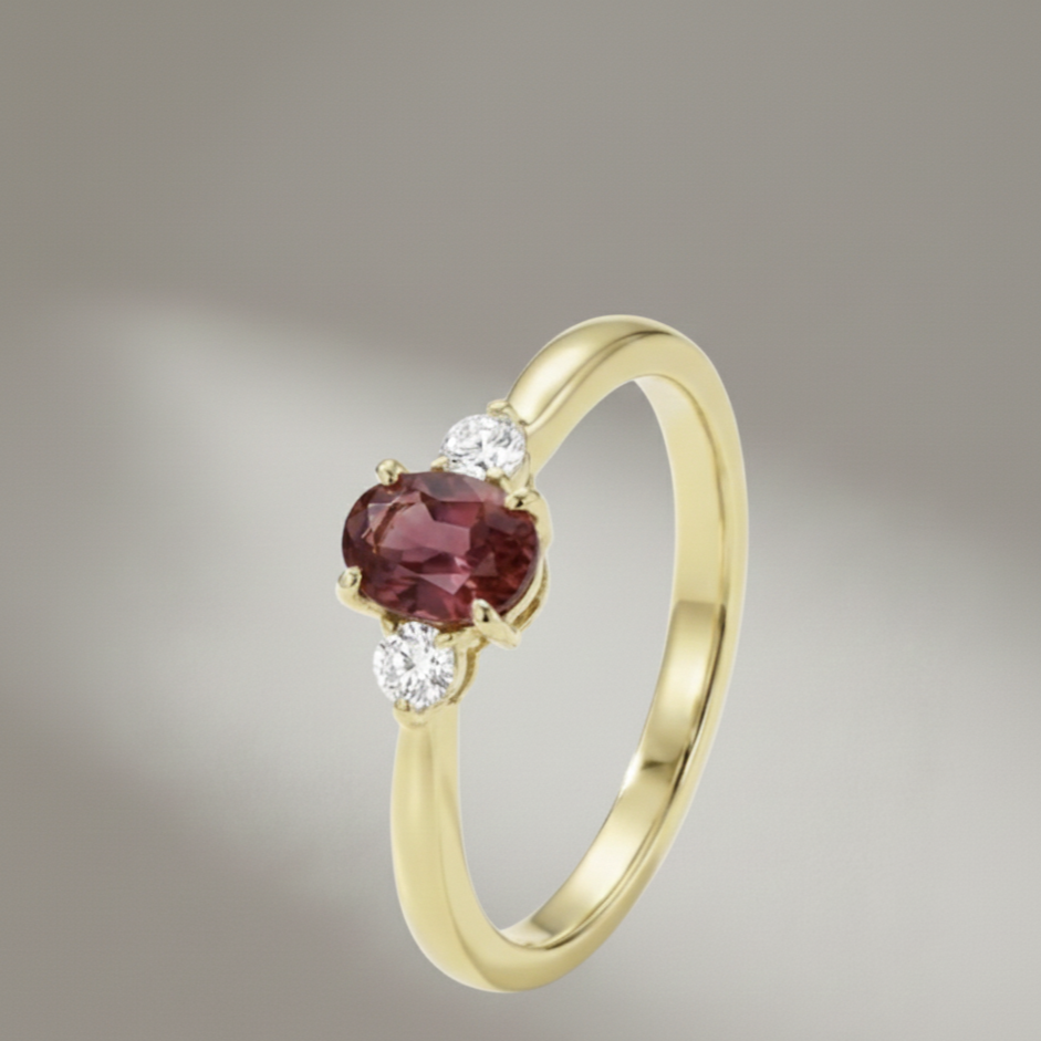 Oval pink tourmaline three stone ring with two diamond accents in polished 14k yellow gold from Brilliant Fine+Custom Jewelry.