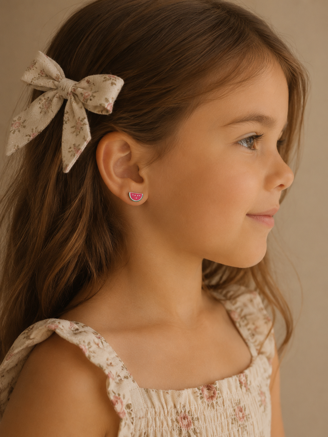 A young girl wearing watermelon enamel stud earrings from Brilliant Fine+Custom Jewelry