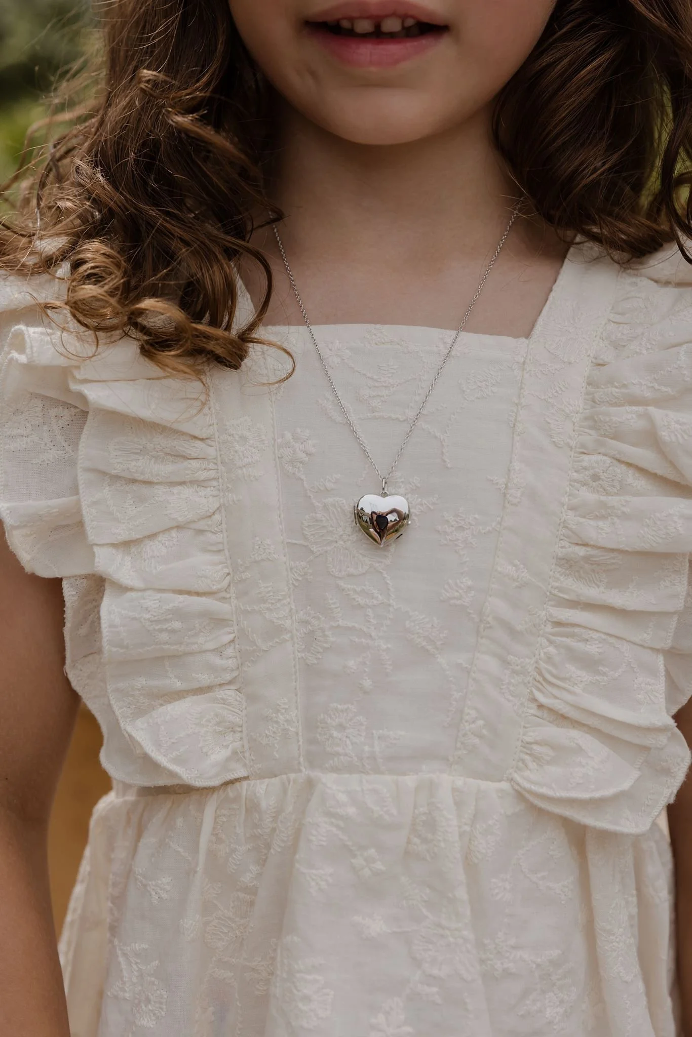 A young girl with curly brown hair is wearing a sterling silver heart pendant on a sterling silver rope chain from Brilliant Fine+Custom Jewelry in Roswell, Georgia.