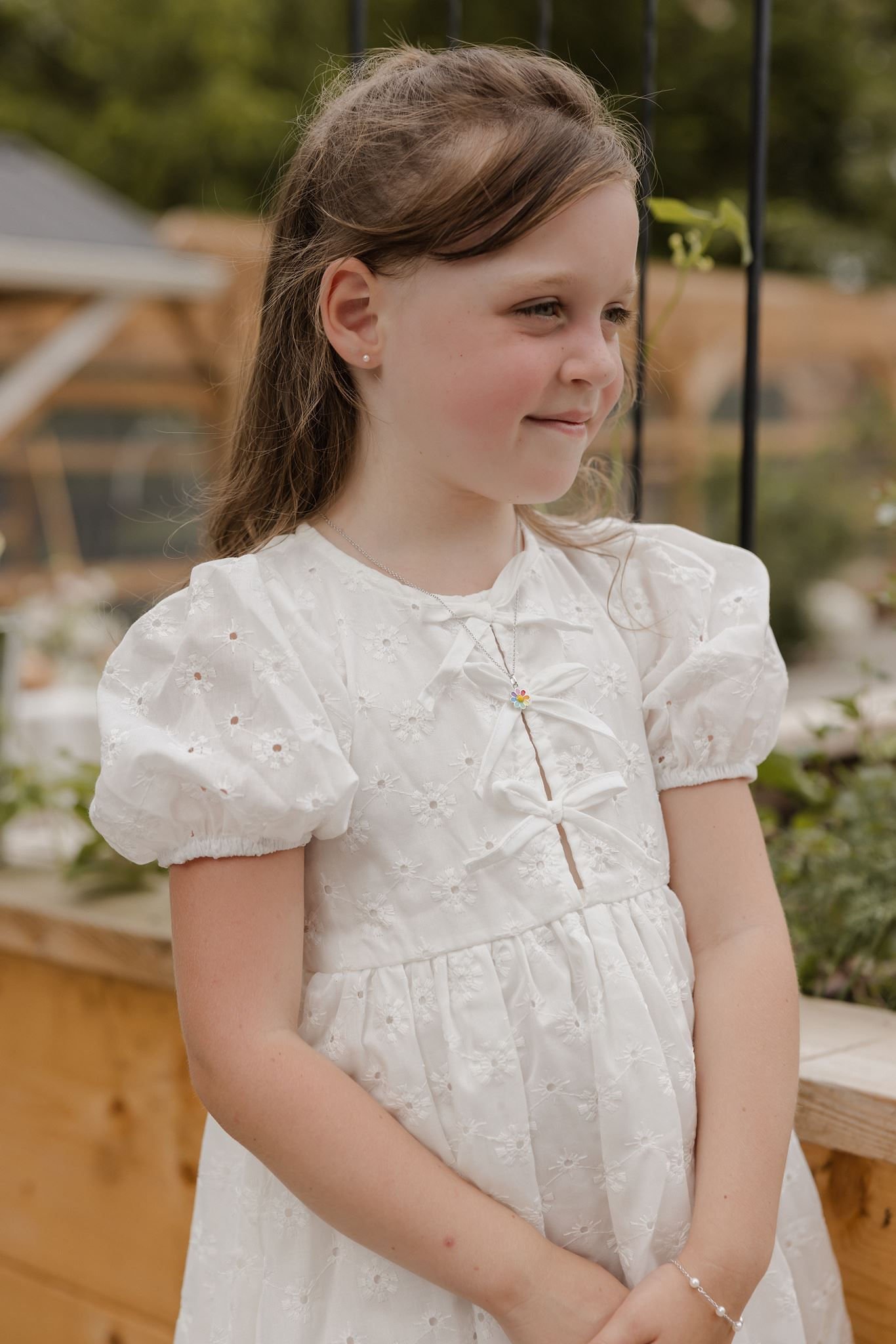 A young girl looks toward the distance. She is wearing a white dress and pearl stud earrings from Brilliant Fine+Custom Jewelry, a perfect first jewelry piece and meaningful keepsake for young girls.