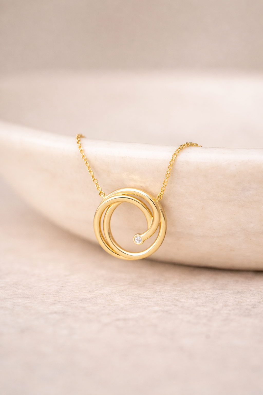 A close up image of our 14k yellow gold swirl necklace with a single natural diamond on a gold chain from Brilliant Fine+Custom Jewelry