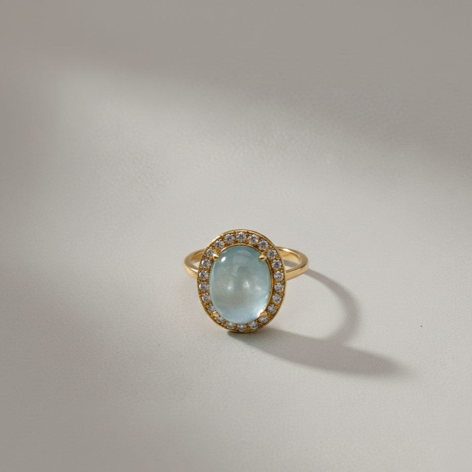 A 14k yellow gold ring with 4.5 carat natural cabuchon blue topaz center stone, encircled by a halo of natural diamonds from Brilliant Fine+Custom Jewelry.