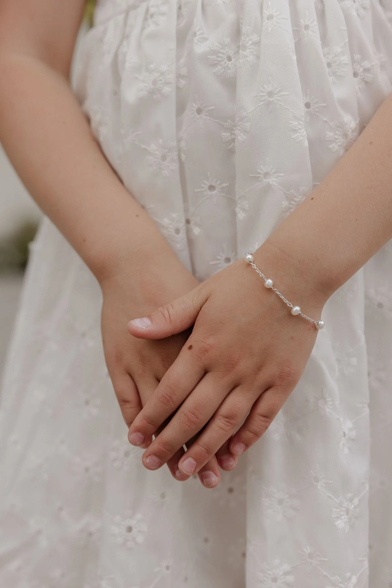 A close up of a young girl's hands, on her wrist is a Pearl Station Bracelet in Sterling Silver from Brilliant Fine+Custom Jewelry in Roswell, Georgia.