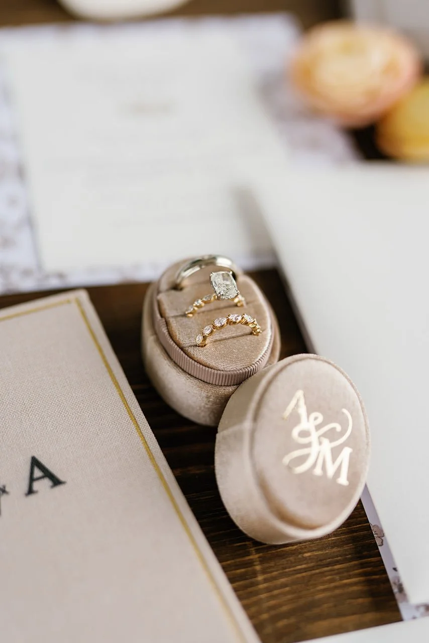 Three rings placed in a ring stack case, one wedding band, one engagement ring with an emerald cut diamond, and a seven-stone half-band from Brilliant Fine+Custom Jewelry.