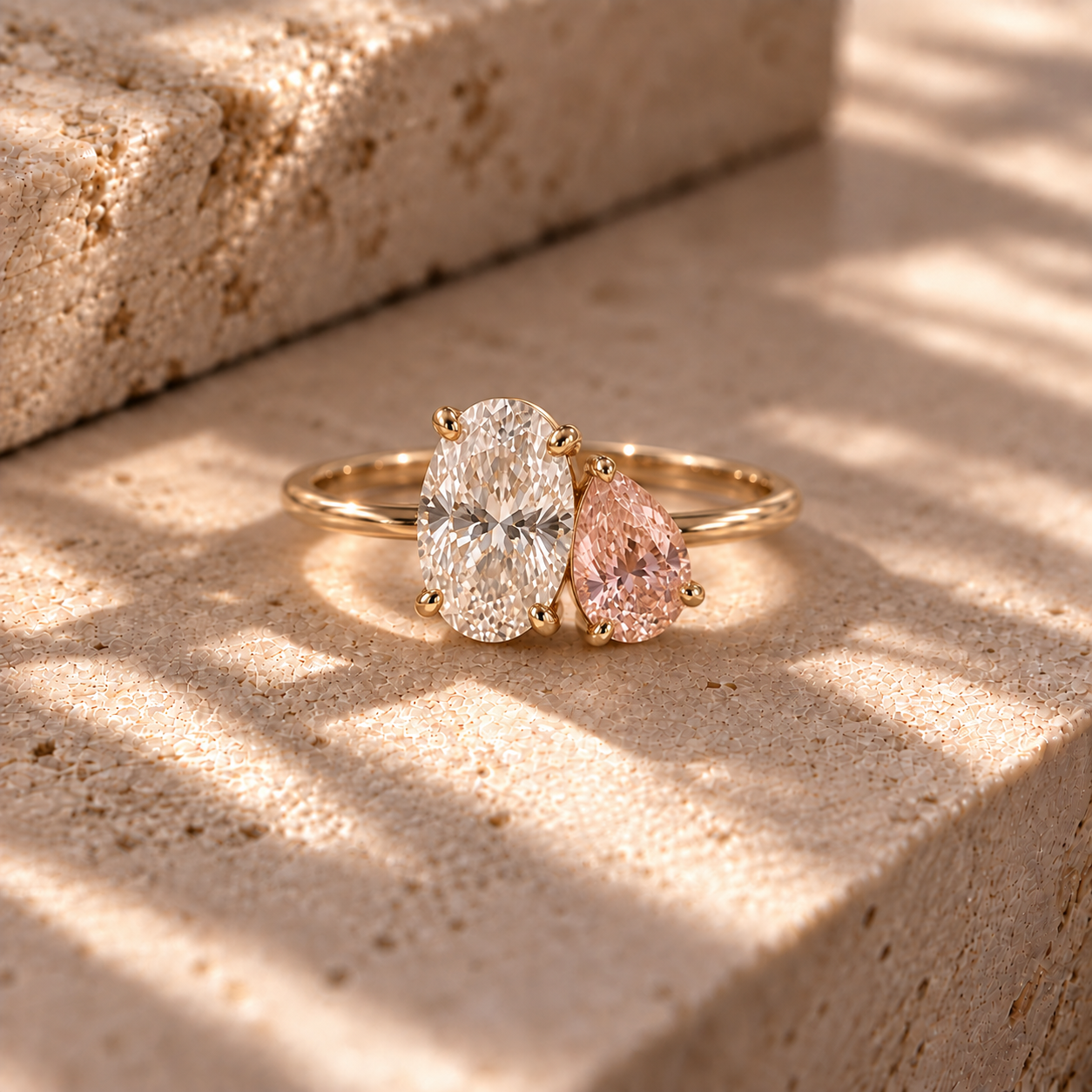 A custom two-stone gold ring with an oval diamond paired next to a triangle-cut pink birthstone from Brilliant Fine+Custom jewelry.