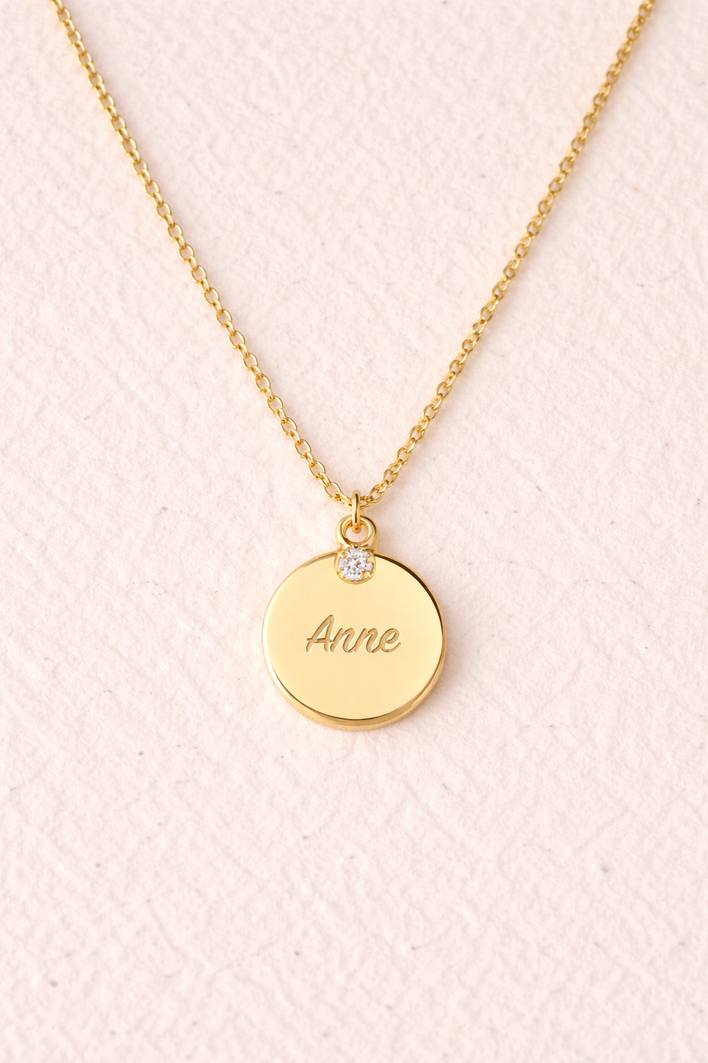 An engravable disc pendant with a 3mm bezel-set cubic-zirconia stone on a 14k yellow gold chain from Brilliant Fine+Custom Jewelry