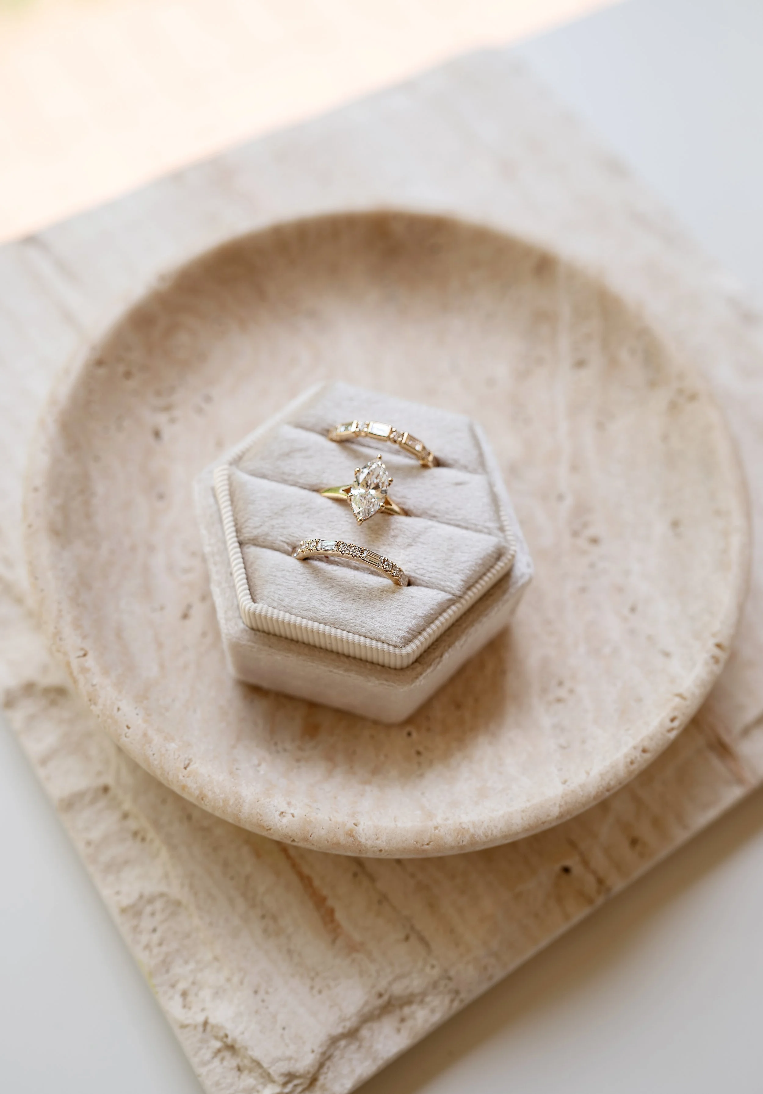 Three gold rings in a ring holder showing an example ring stack. The top and bottom rings are simple, elegant bands, with the middle ring an extravagant engagement ring with a marquise-cut diamond set in yellow gold by Brilliant Fine+Custom..