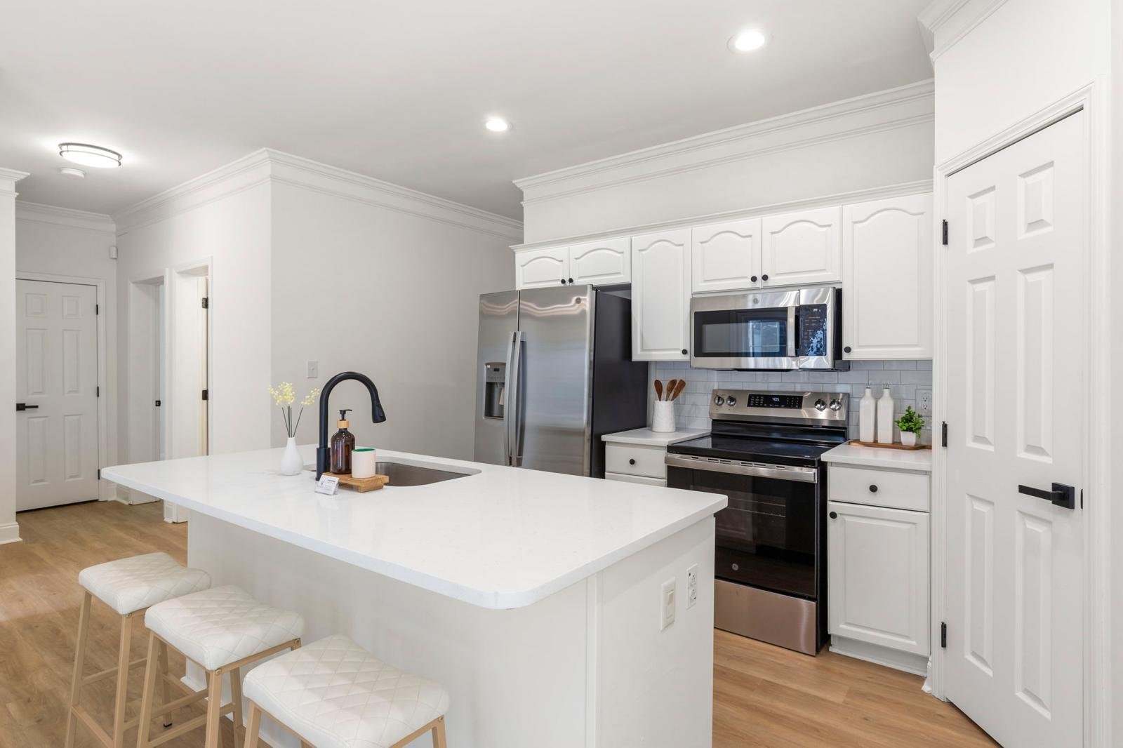 Modern kitchen with white cabinets, stainless steel appliances, a white island with bar stools, and light wood flooring.
