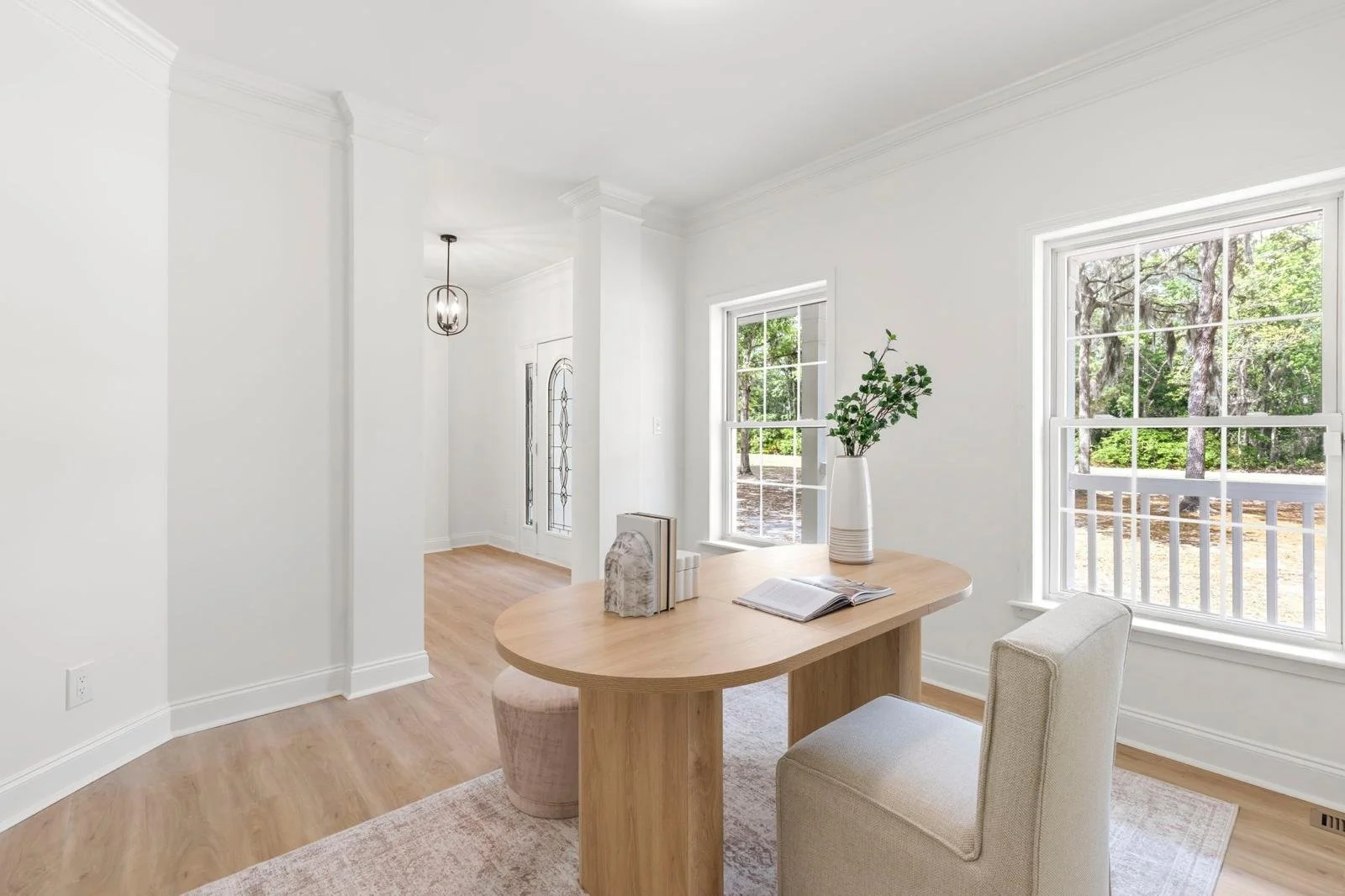 Bright dining space with a wooden table, a beige chair, and a large window showing a green outdoor view.