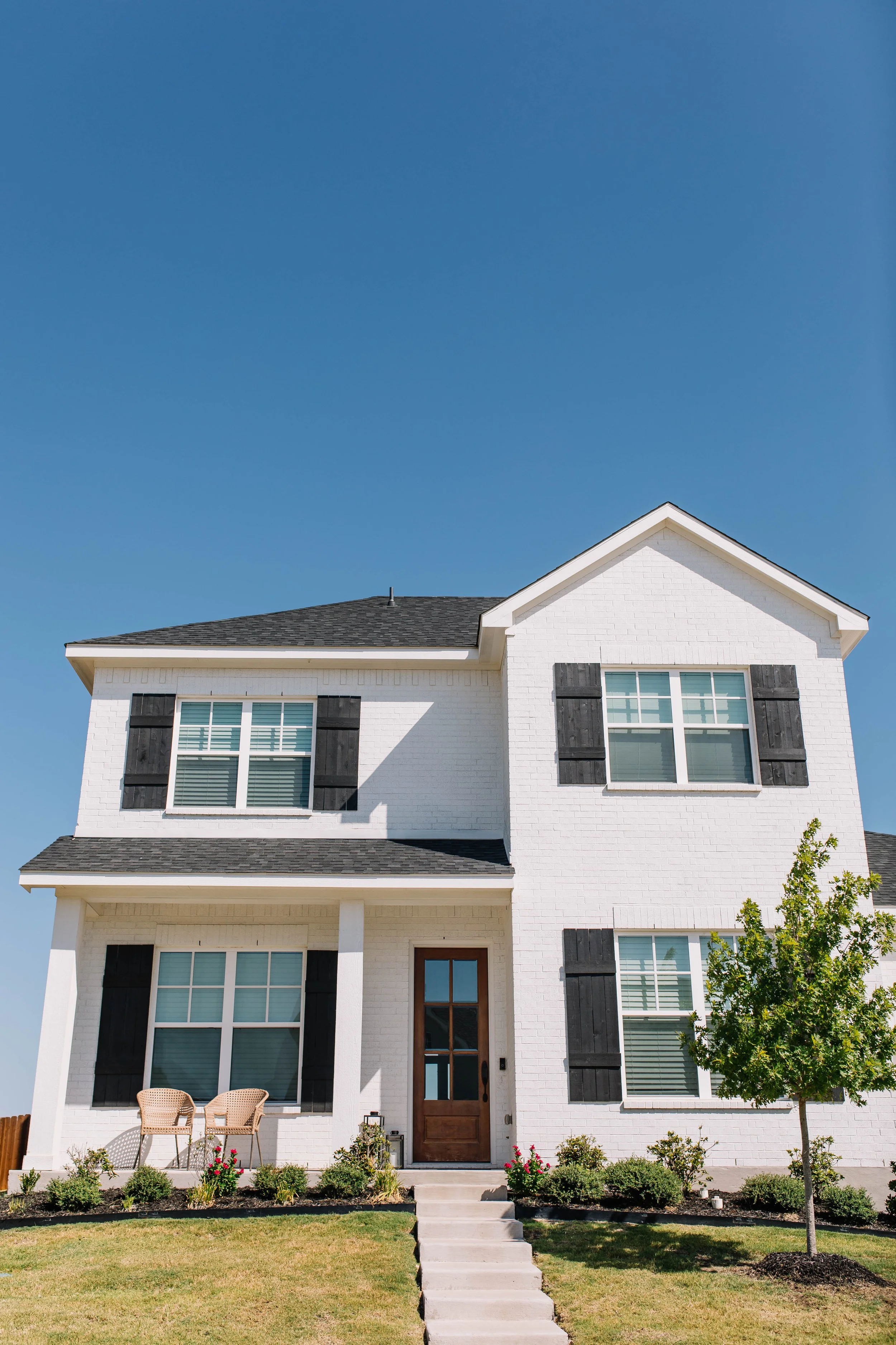 A two-story white brick home with brown wooden shutters