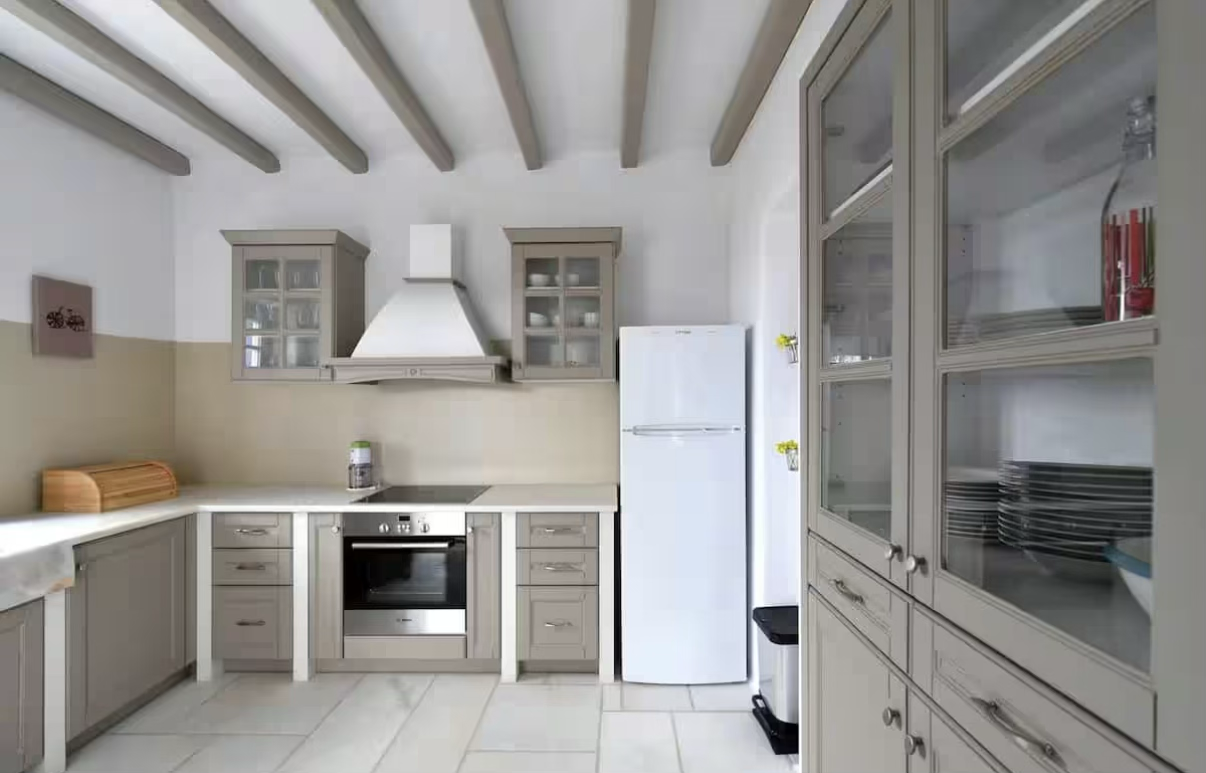 Kitchen with beige cabinets, white walls, gray exposed ceiling beams, a white refrigerator, a built-in oven, glass-front upper cabinets, and a stovetop with a white range hood.