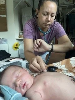 Female healthcare professional using a stethoscope to examine a sleeping baby's chest in a clinical setting.