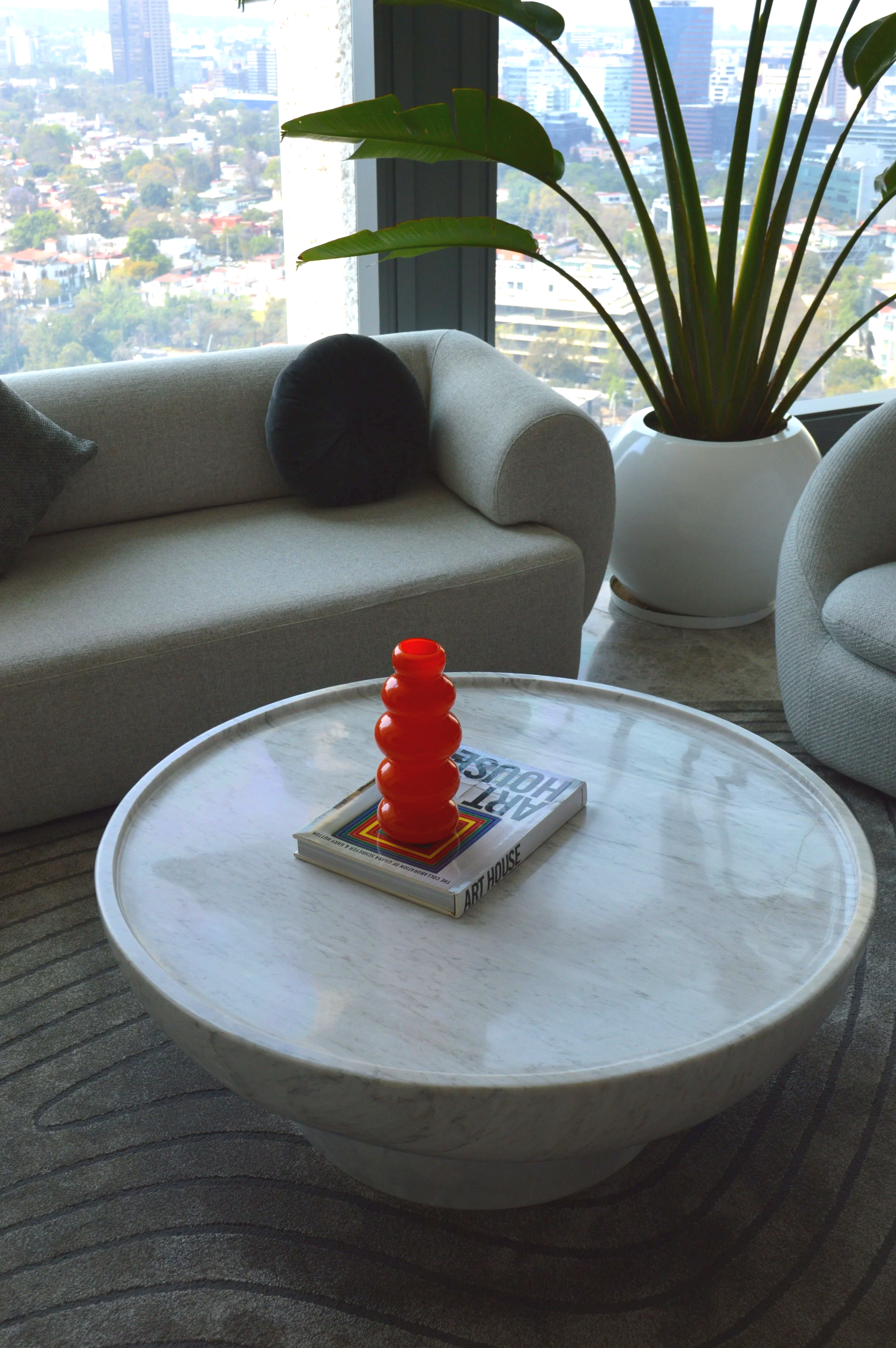 Sala moderna con sofá moderno, plantas grande en macetas blancas elegantes y inimalistas, mesa de centro de mármol con decoración contemporanea ventanas amplias con vista a la ciudad.