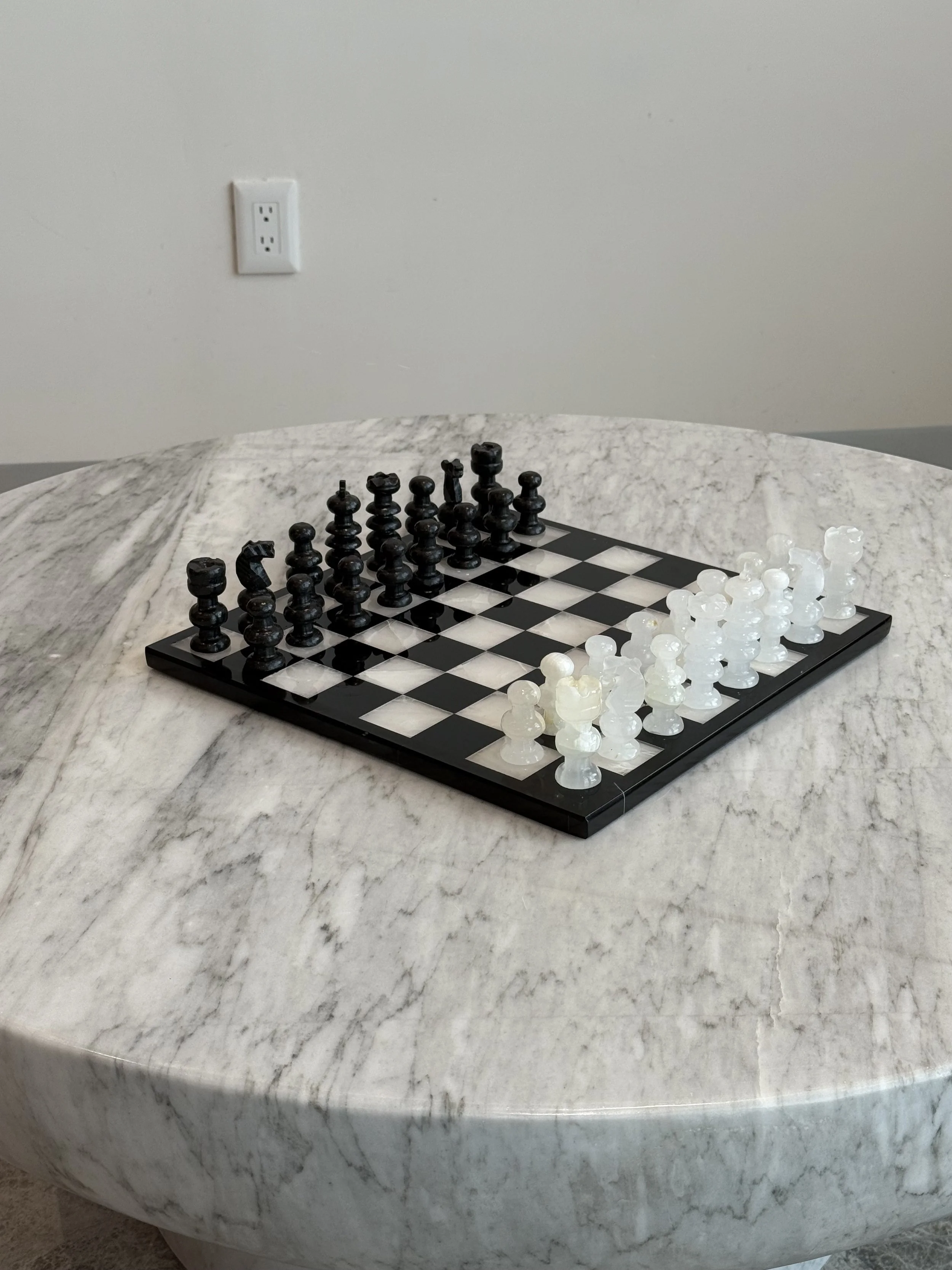 Tablero de ajedrez con piezas blancas y negras en una mesa de mármol.