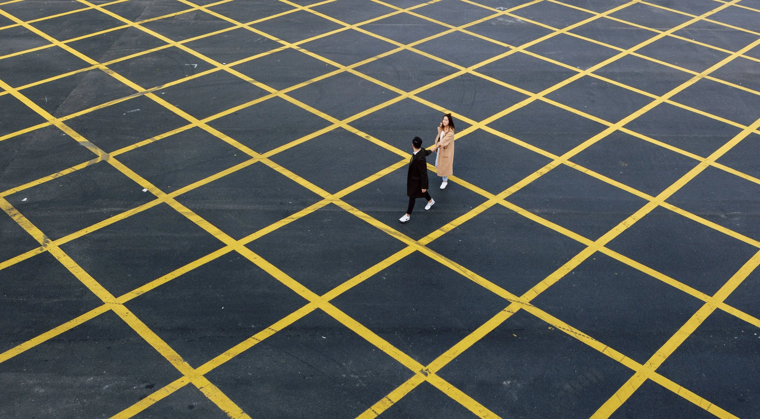 Two people walking on a grid-patterned surface with yellow lines