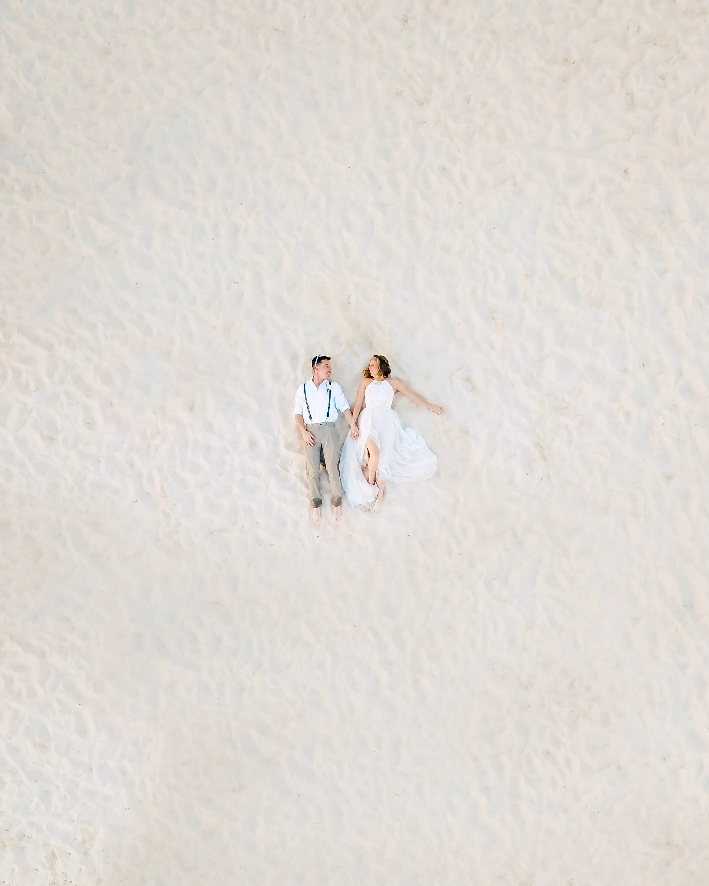 Bride and groom lying on sandy beach, aerial view