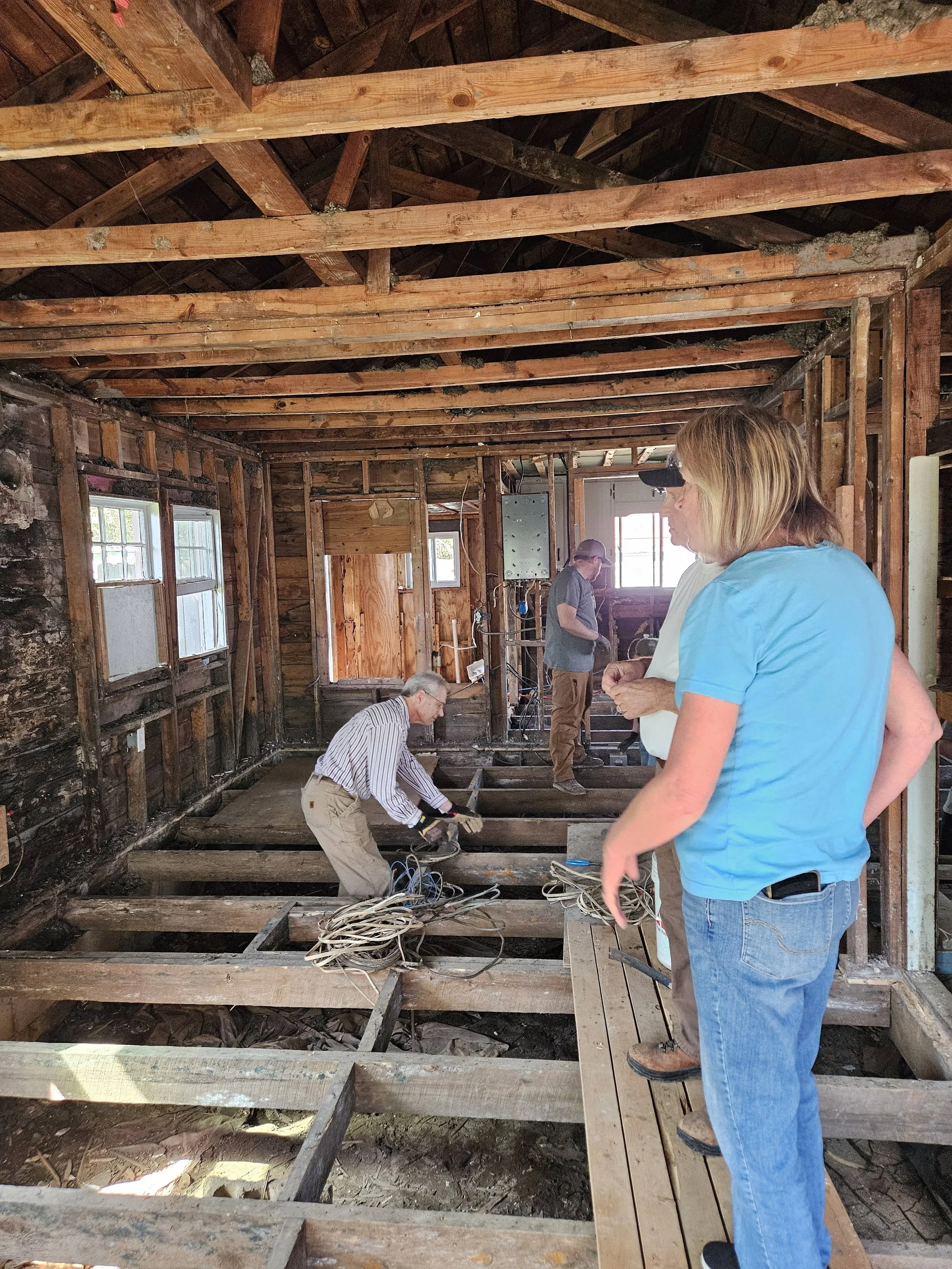 People working on the renovation or repair of a house, removing and replacing the flooring in a room with exposed wooden beams and walls.