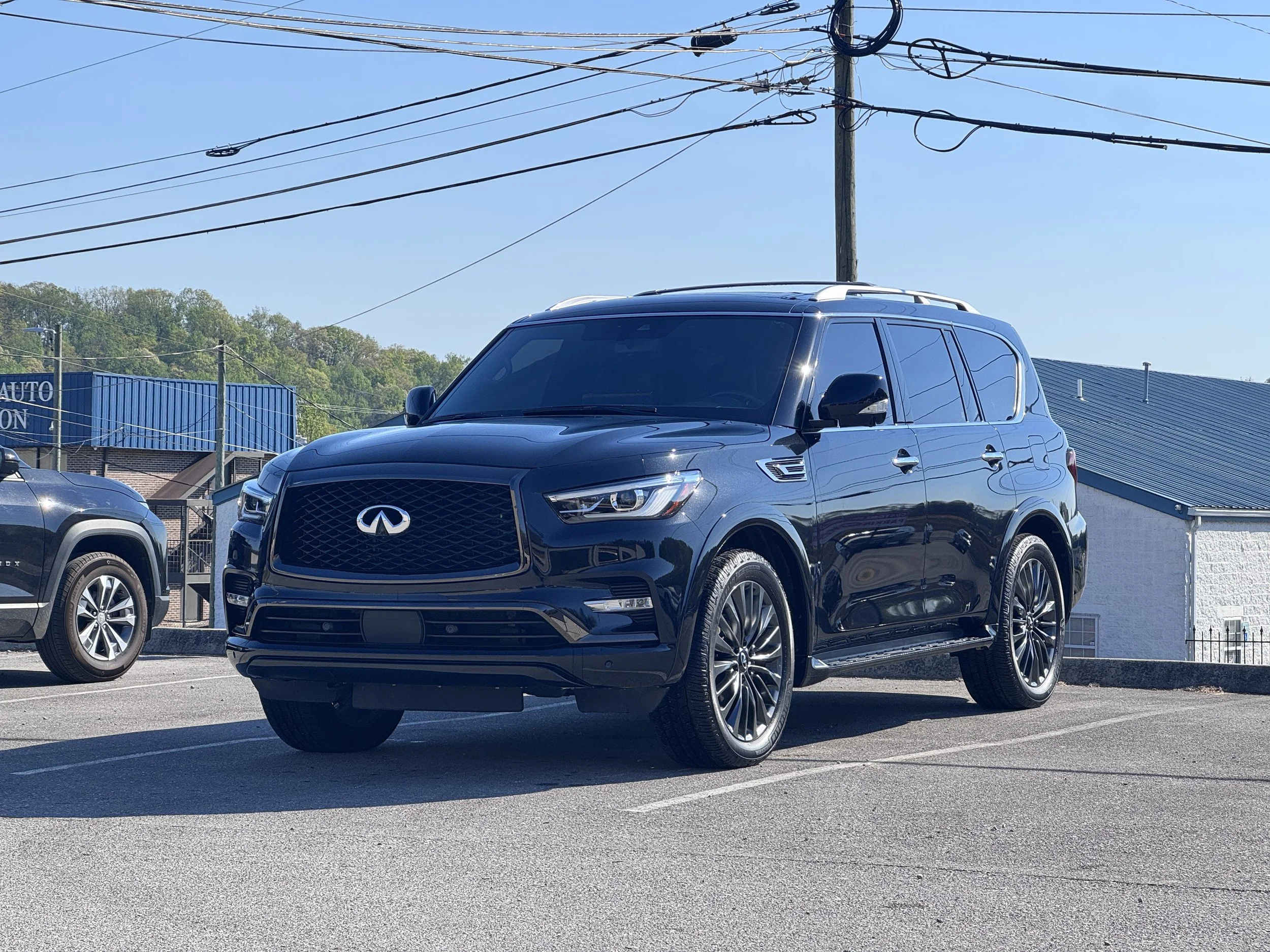 A shiny black SUV parked in a car dealership lot with other vehicles visible around it. There are power lines above and a blue building in the background.