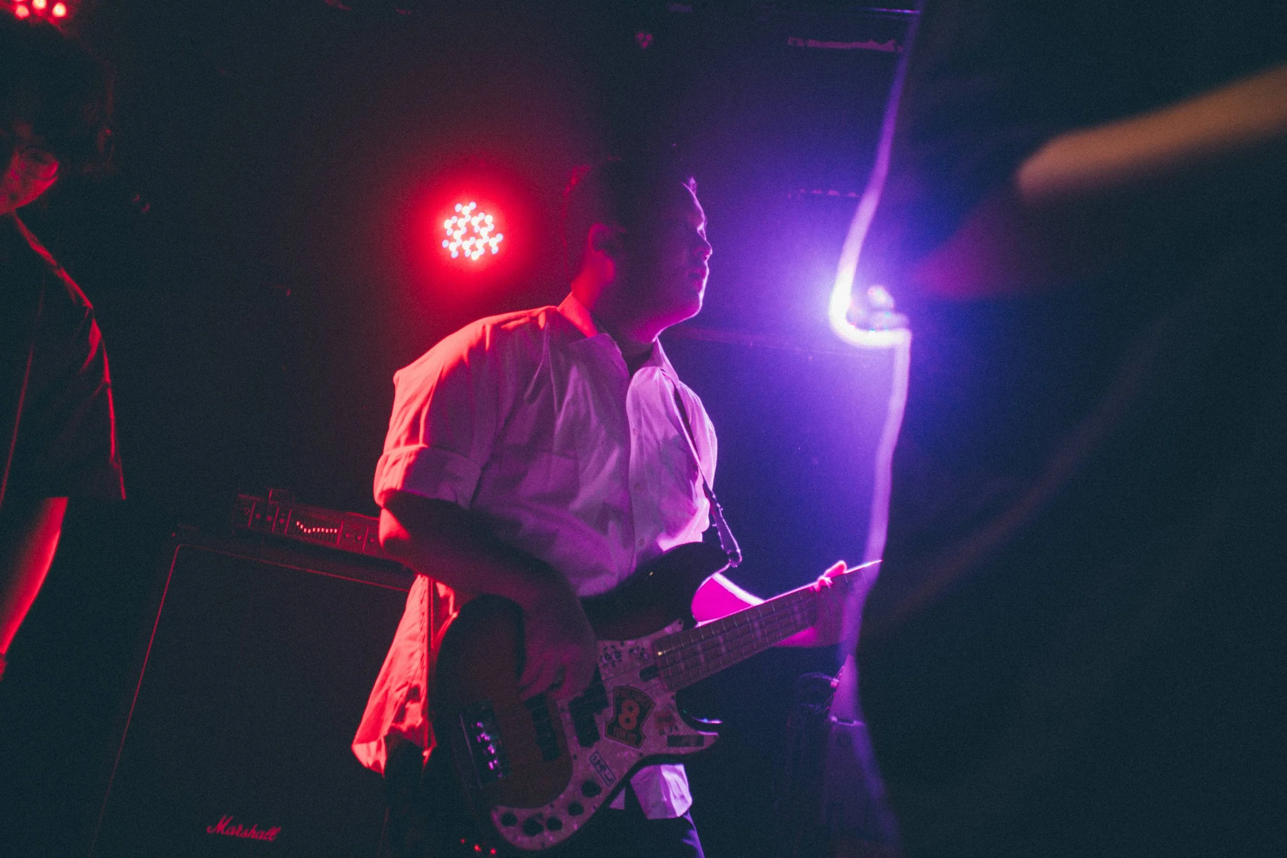 A musician playing an electric guitar on stage, illuminated by colorful stage lights, with a Marshall amplifier in the background.