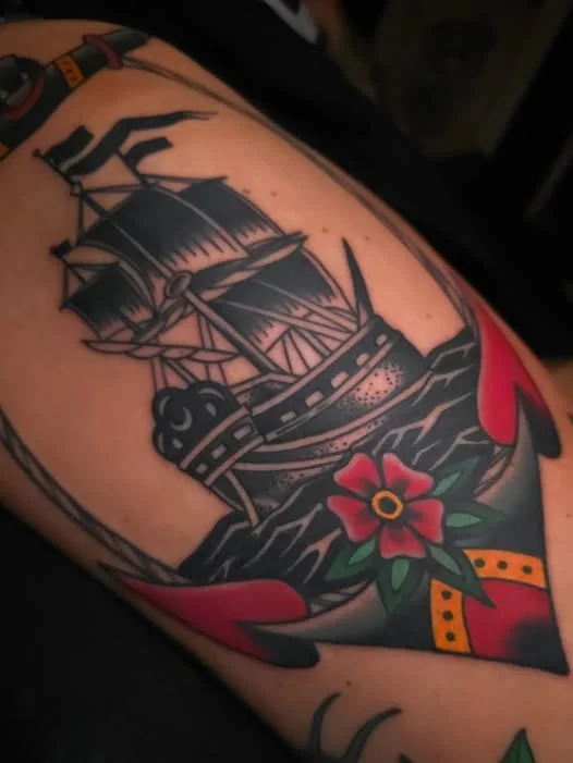 Tattoo of a sailing ship on water, surrounded by stylized red and green elements.