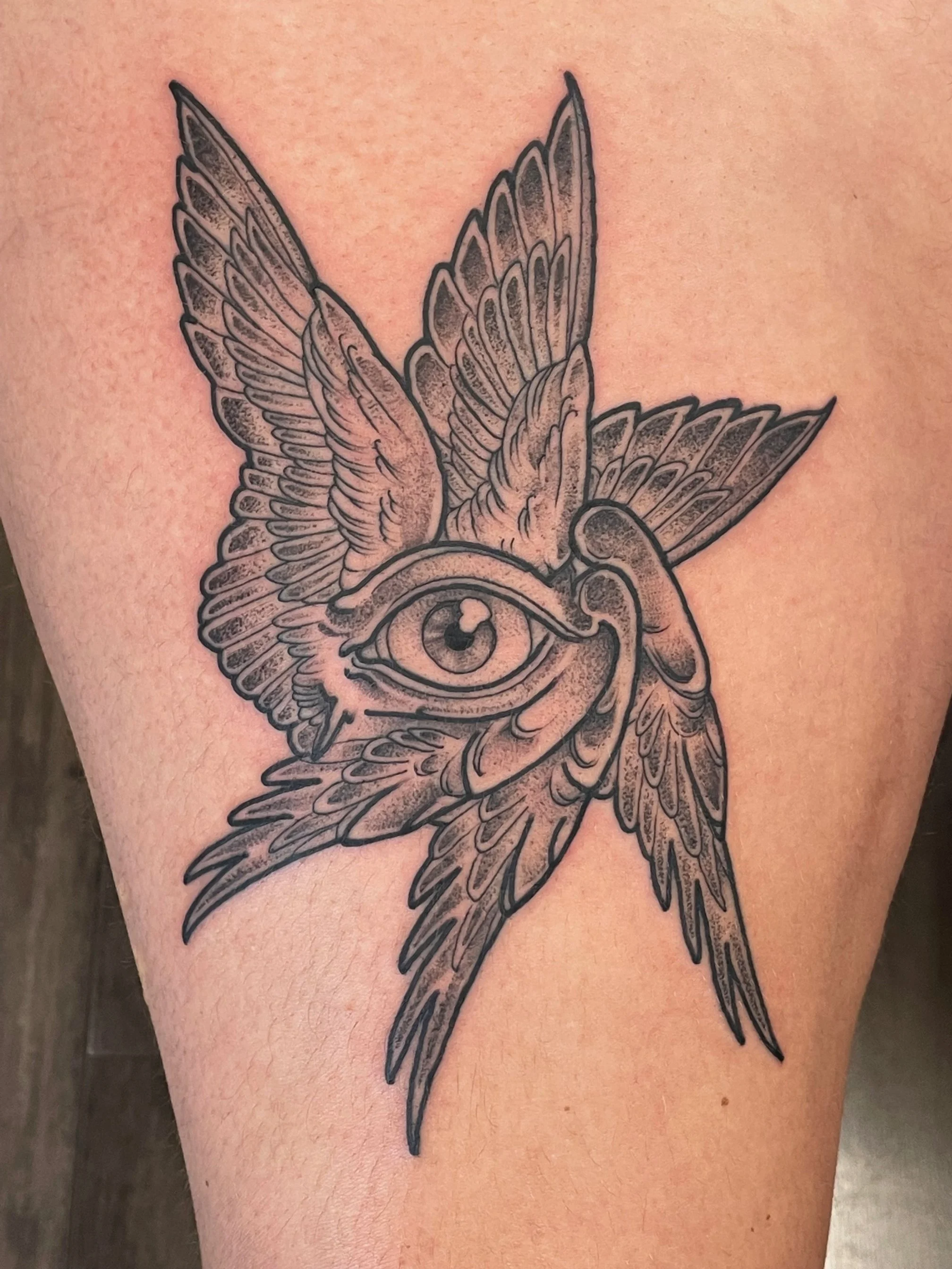 Tattoo of a bird with outstretched wings, featuring a large eye on its body, on a person's skin.