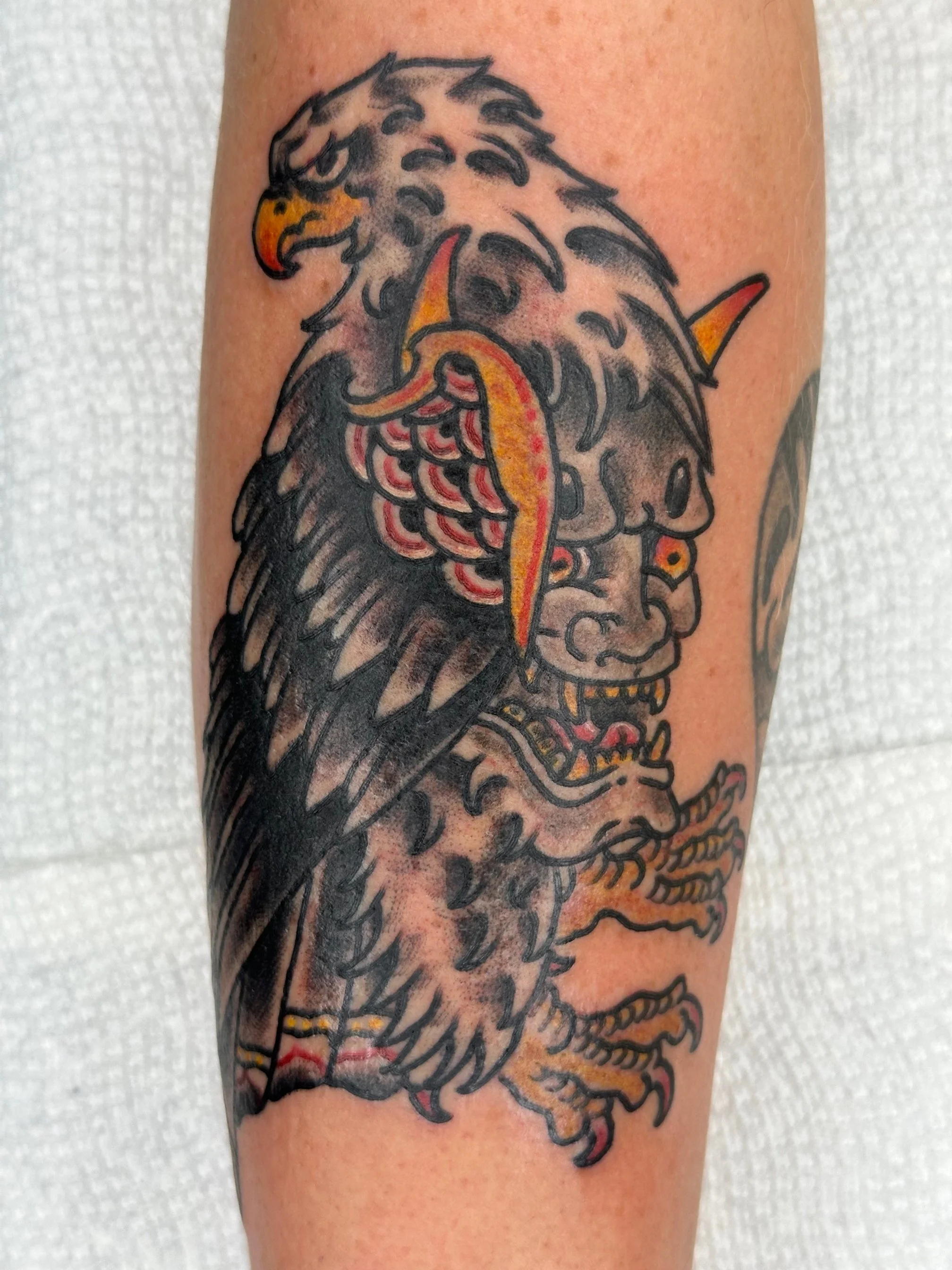 Tattoo of a lion's head combined with a traditional Japanese mask, with bold black outlines, red and yellow accents, and intricate details.